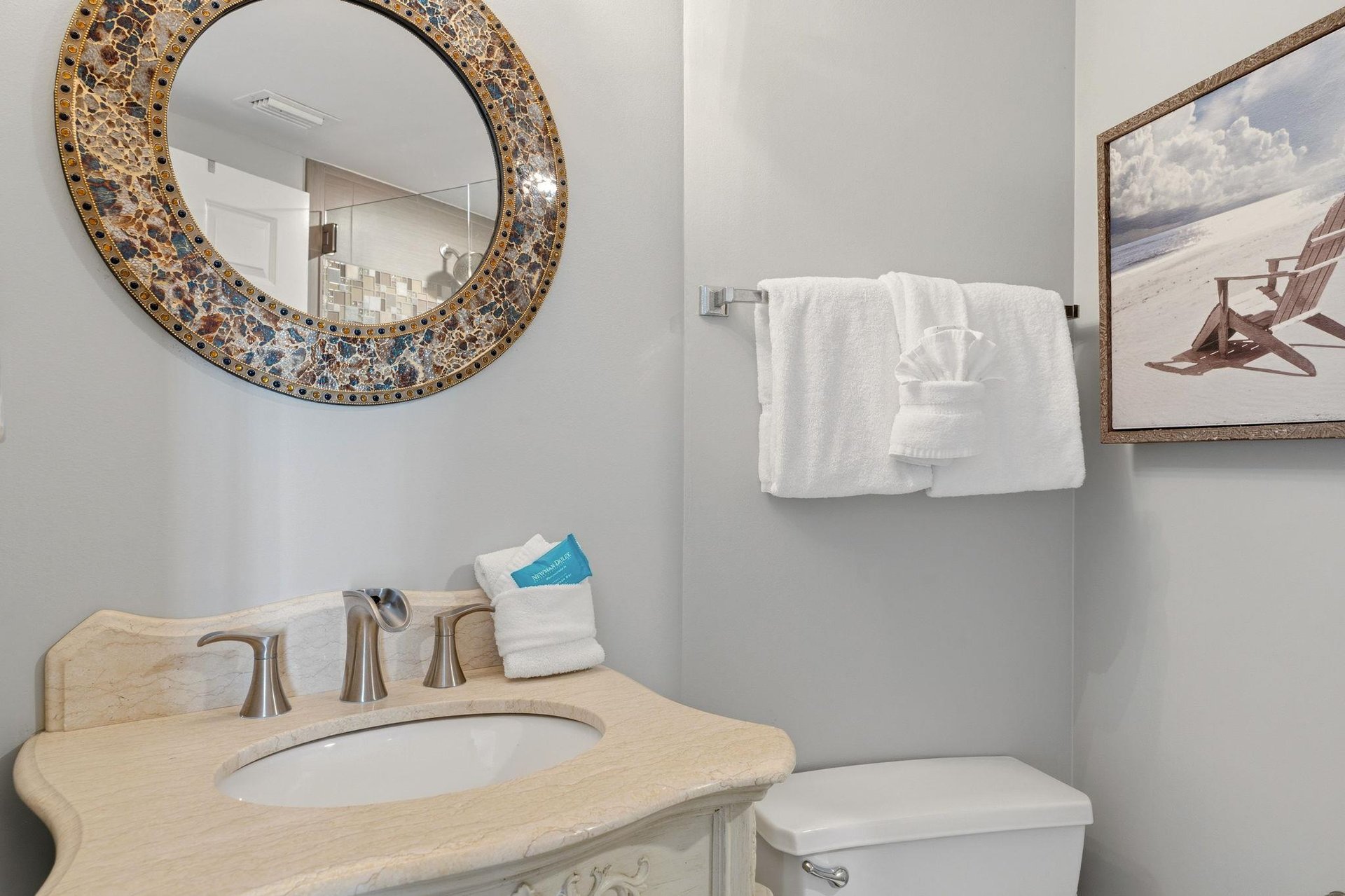 Refresh in your elegantly appointed bathroom featuring a stunning mosaic mirror, plush towels, and coastal artwork creating a spalike retreat.