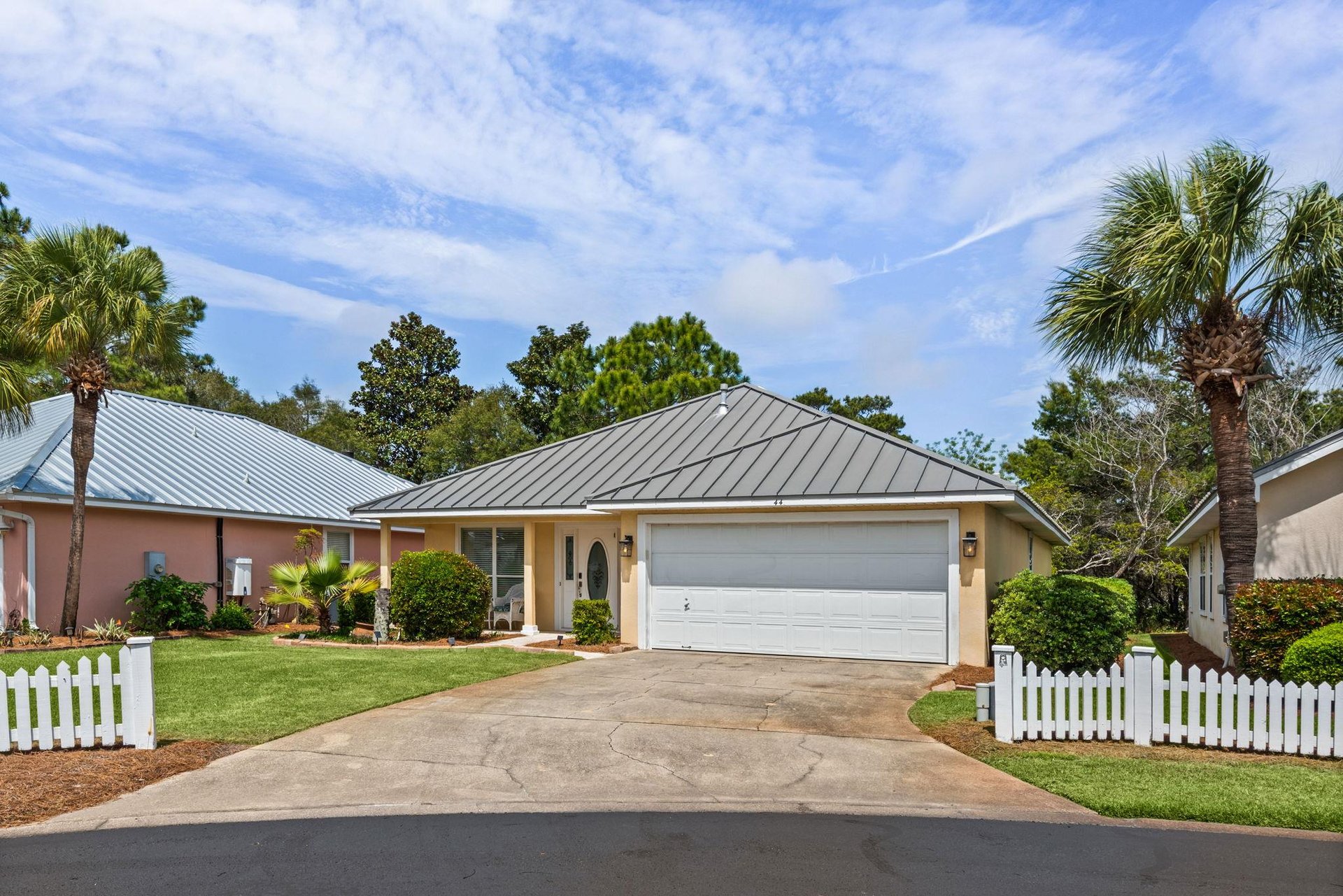 Charming singlestory home with metal roof nestled among palm trees in peaceful residential neighborhood.