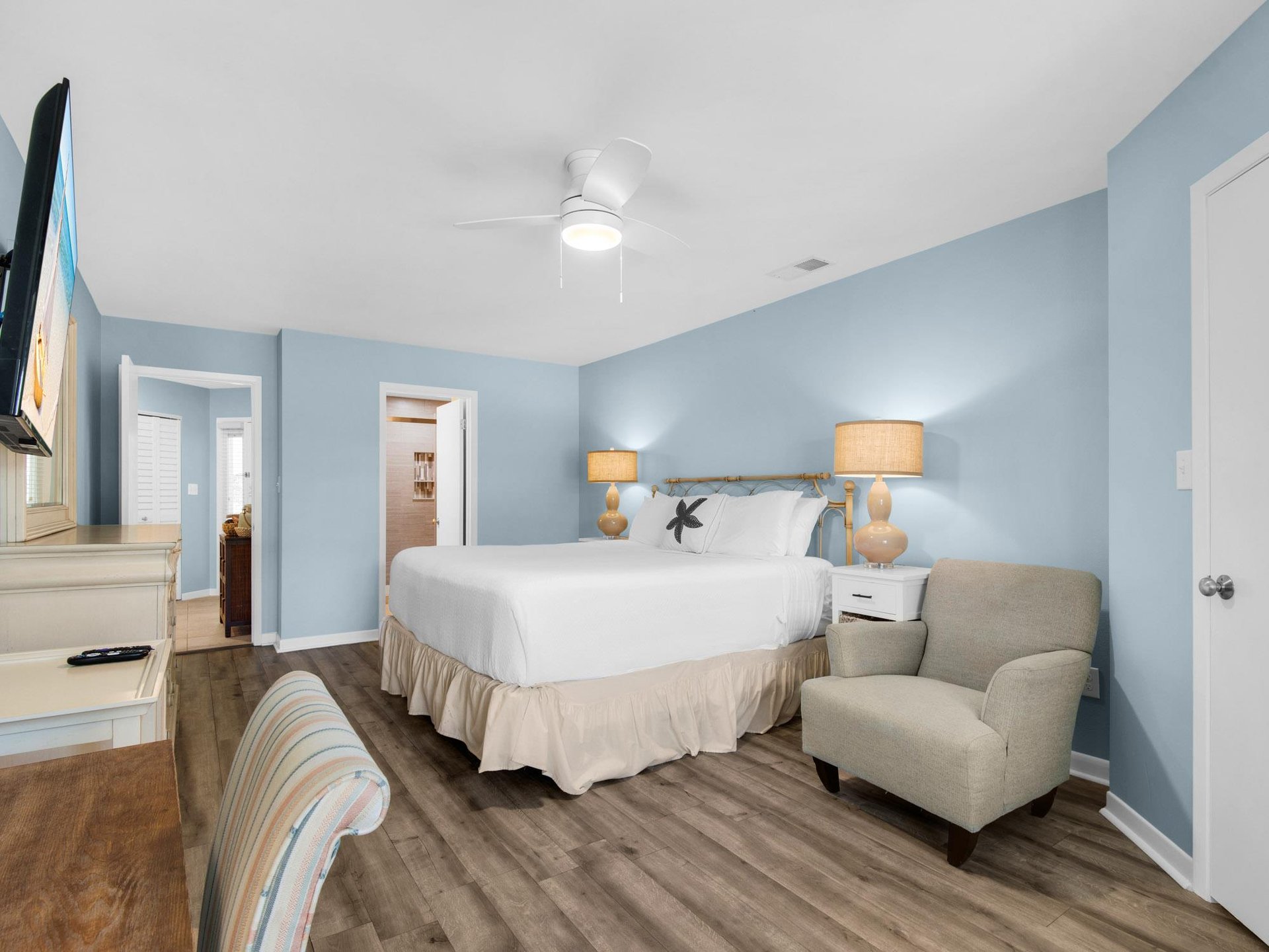 Unwind in your serene coastal bedroom with soft blue walls, plush king bed, and cozy seating area perfect for morning coffee or evening relaxation.
