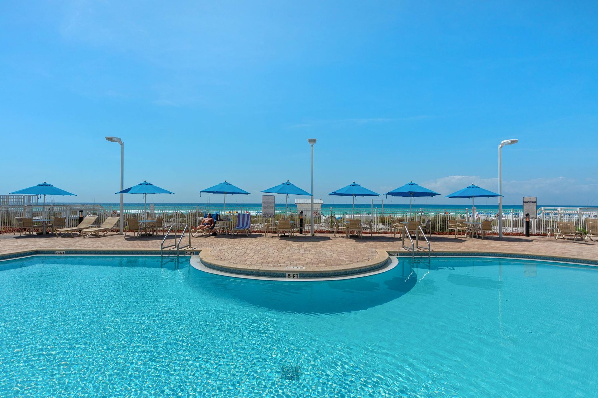 Sparkling pool with beachfront access featuring turquoise umbrellas and lounge chairs overlooking pristine sandy shores.