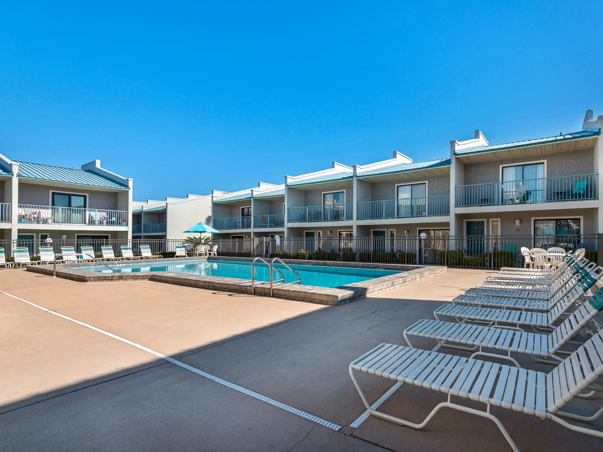 Multistory vacation rental complex featuring a central swimming pool surrounded by modern accommodations with balconies and outdoor seating areas.