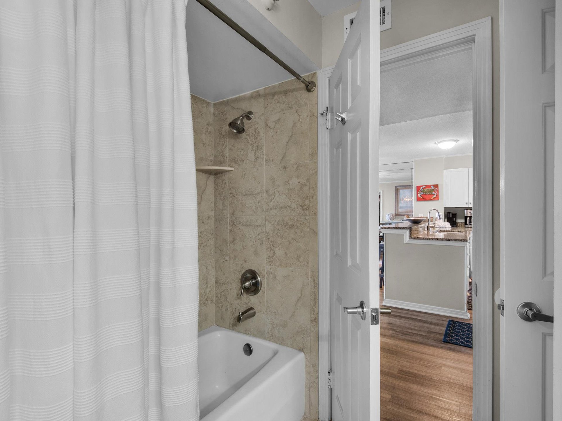 Your private bathroom features a tubshower combo with sleek marblestyle tile, crisp white fixtures, and a view into the fully equipped kitchen beyond.