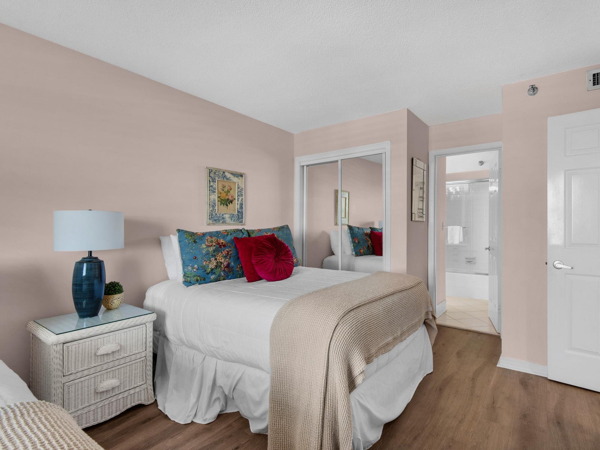 Your serene bedroom retreat features soft pink walls, plush bedding with vibrant floral pillows, and convenient access to your private ensuite bathroom.