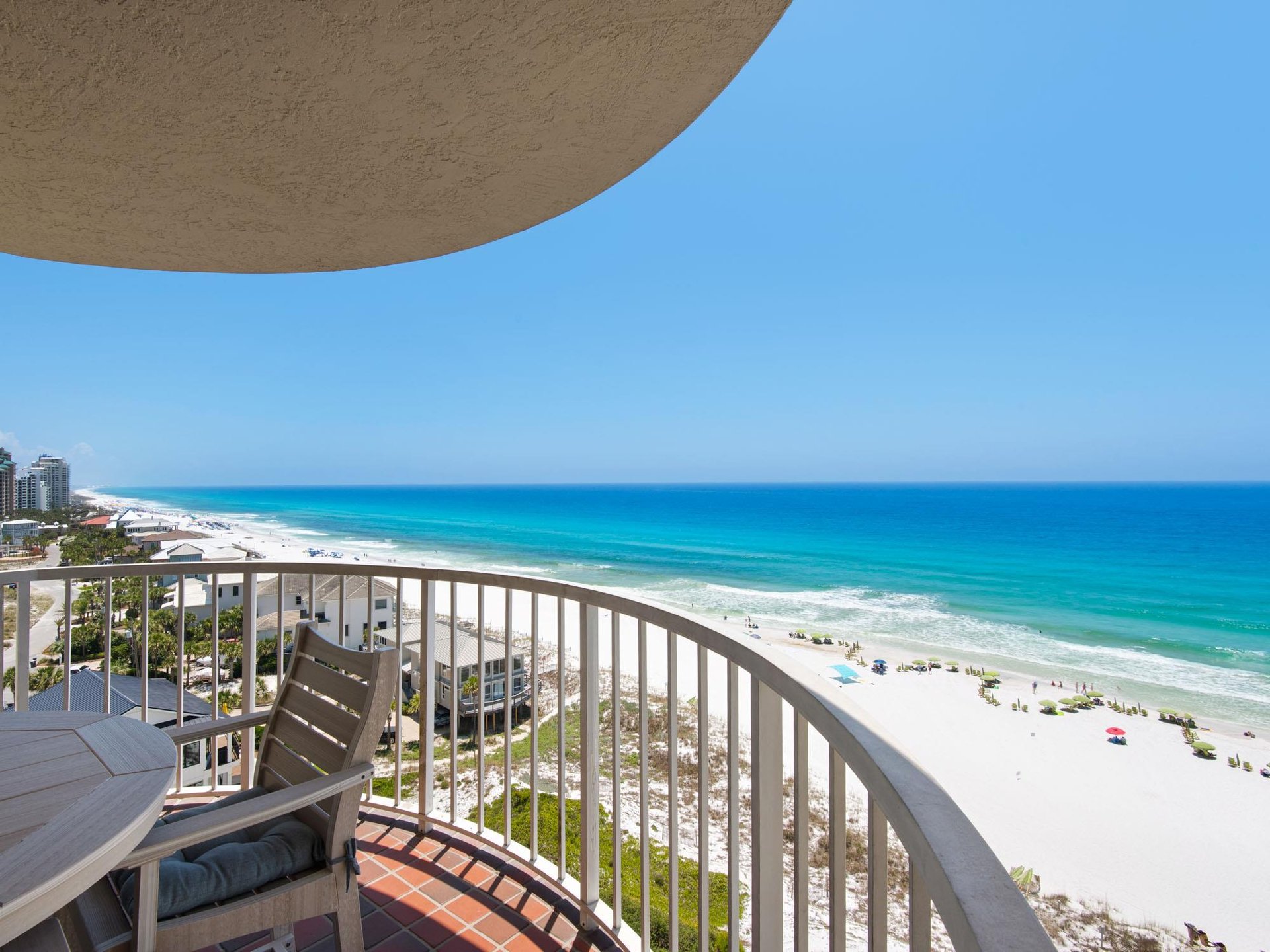 A curved balcony overlooks a pristine white sand beach and turquoise Gulf waters, offering an elevated coastal perspective for arrival at this beachfront property.