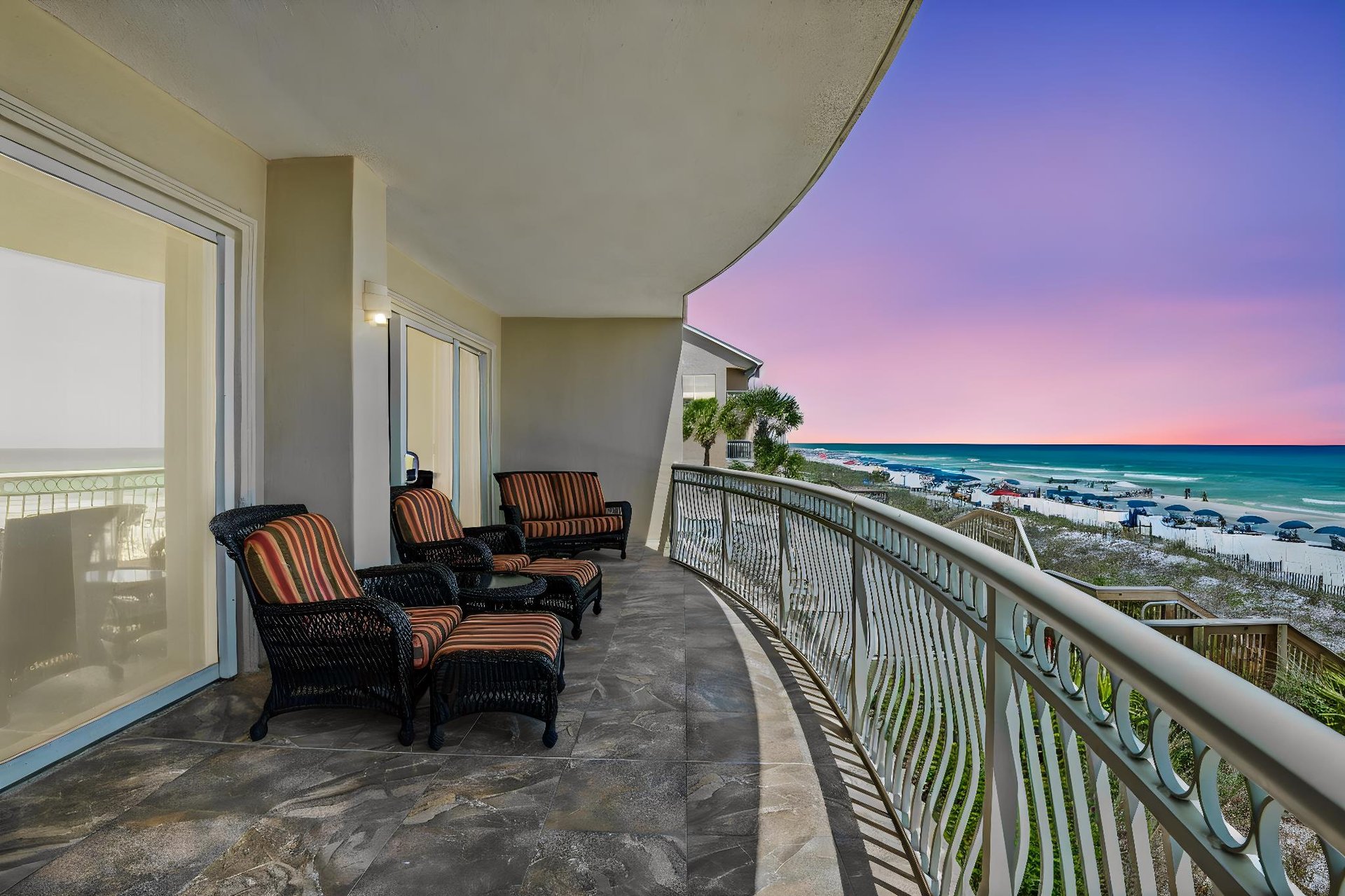 Spacious beachfront balcony with comfortable seating overlooking white sand and turquoise waters, perfect for sunset cocktails after a beach day.