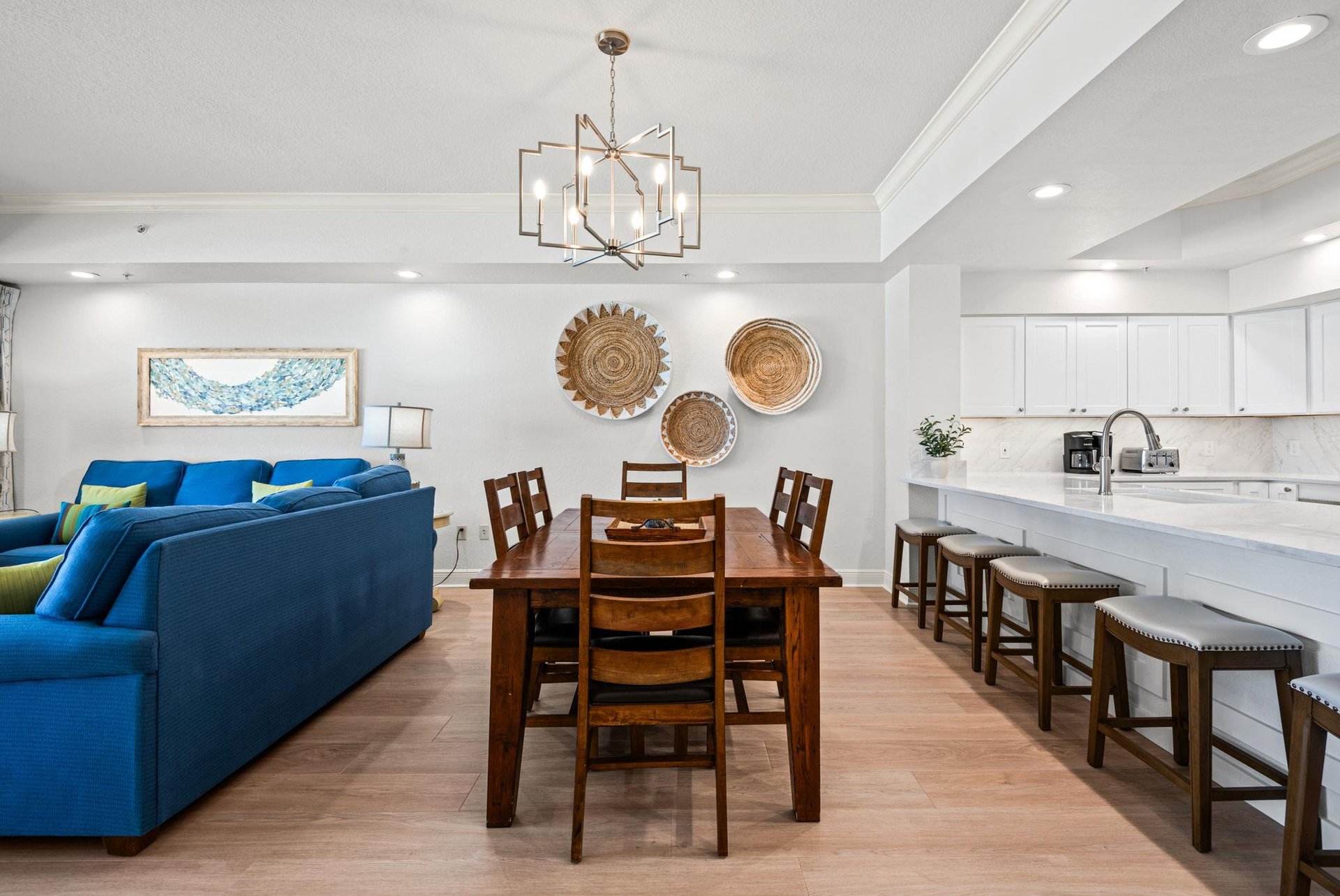 The openconcept living space flows seamlessly from plush blue sofas to a warm wooden dining table and sleek white kitchen, perfect for gathering.