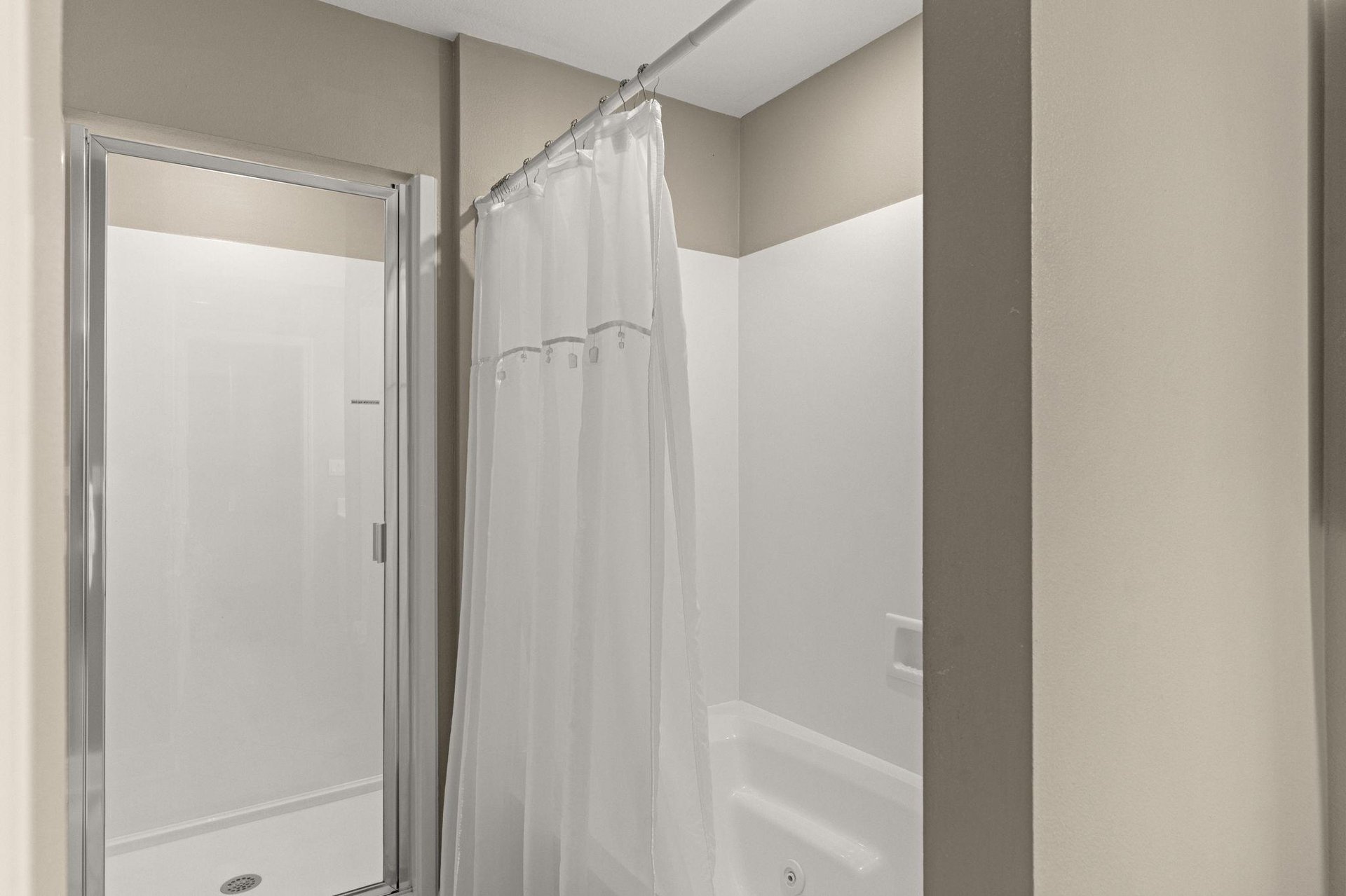 A modern bathroom featuring a spacious tub with crisp white curtain and a separate glassenclosed shower.