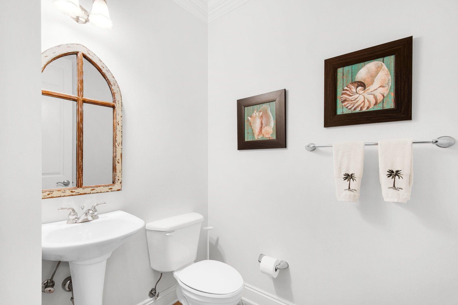 The powder room features coastal accents, soft lighting, and a charming arched mirror.
