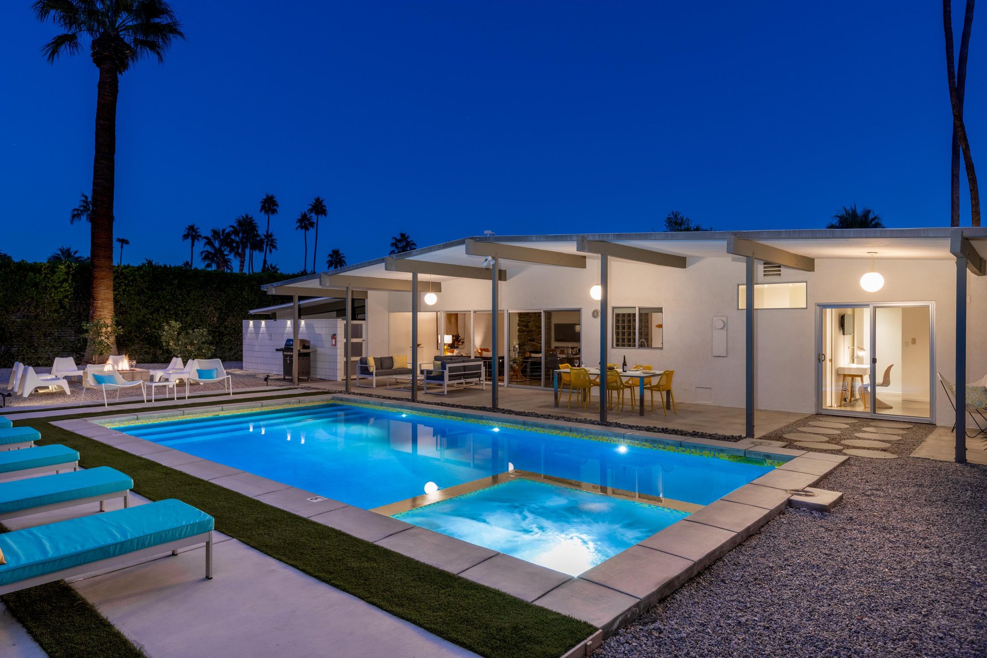 Modern desert retreat featuring illuminated pool and spa surrounded by iconic palm trees under vibrant evening sky.