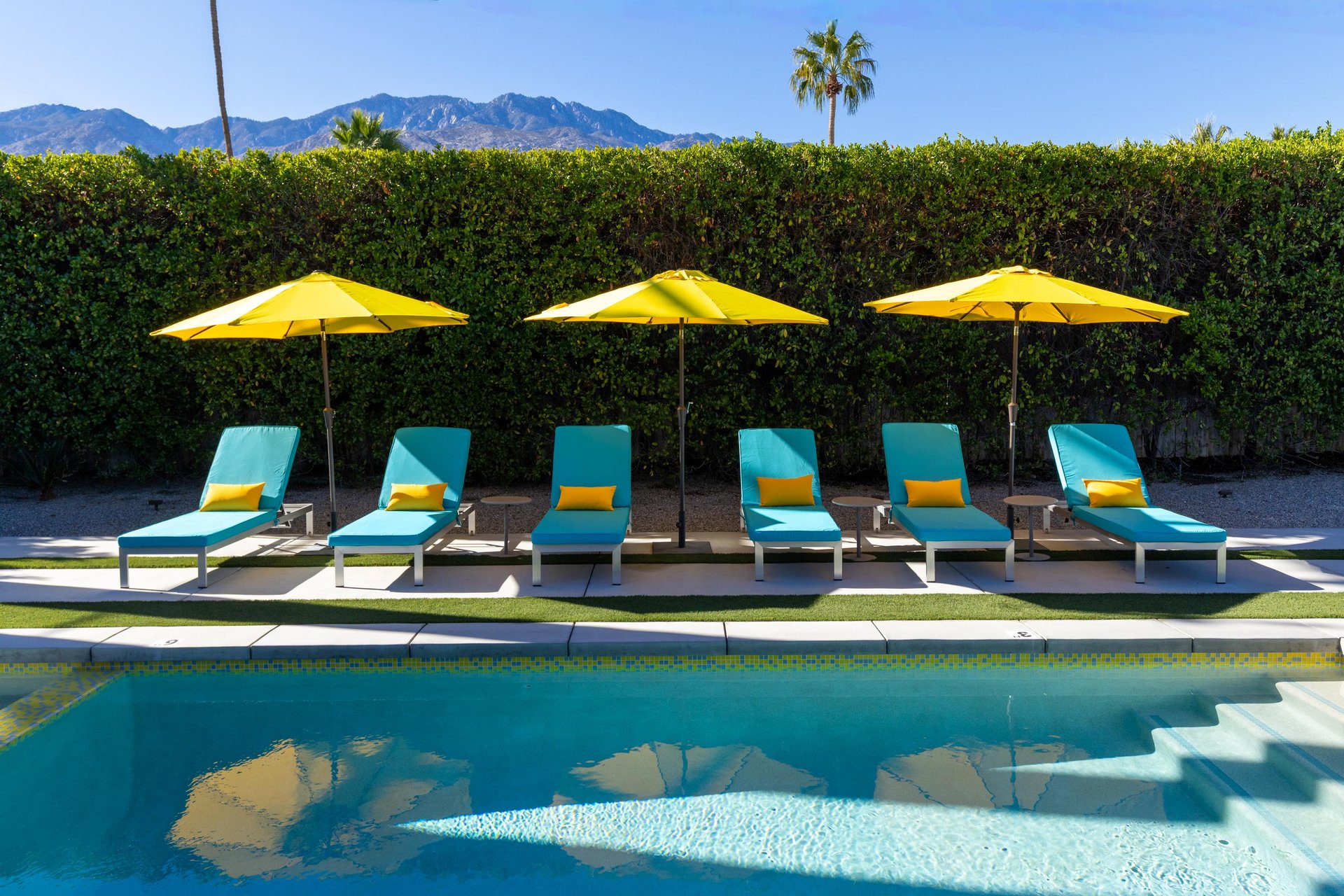 Pristine poolside setting with turquoise loungers and sunny yellow umbrellas, framed by desert mountains for the perfect Palm Springs retreat.