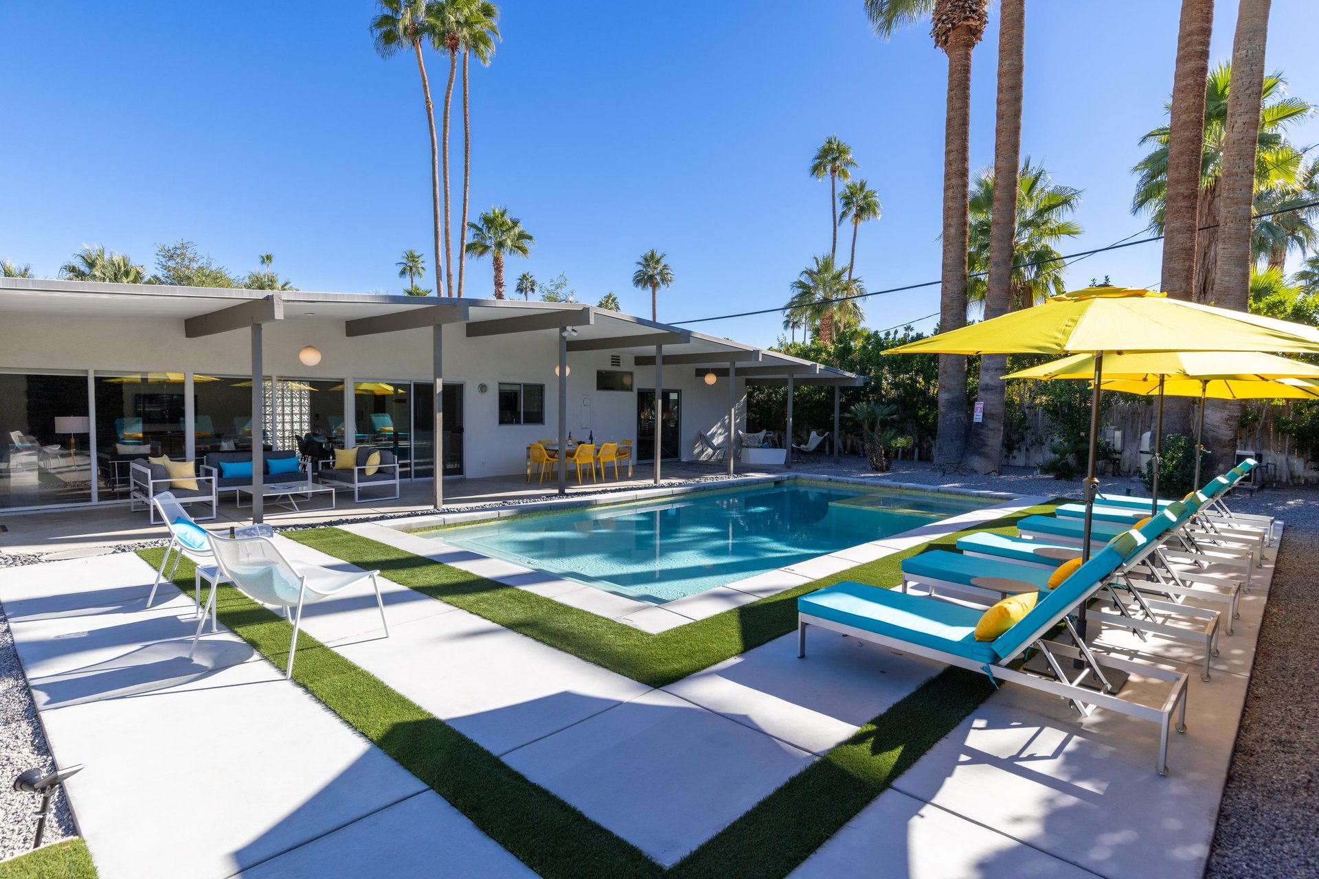 A Palm Springs oasis featuring midcentury modern architecture with pristine pool and towering palm trees.