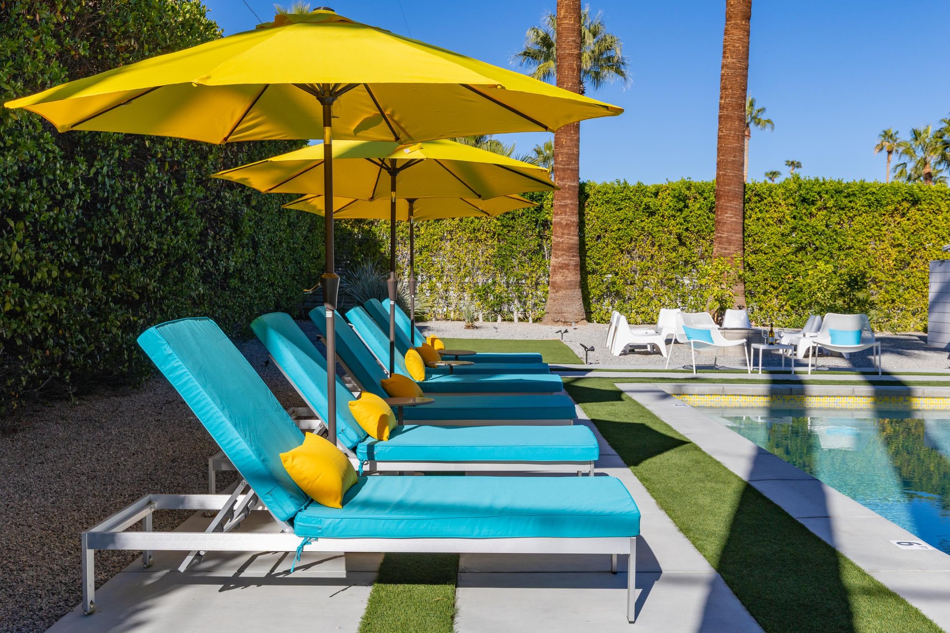Sink into vibrant turquoise loungers beside your private pool, where sunny yellow umbrellas create perfect shade for afternoon relaxation.