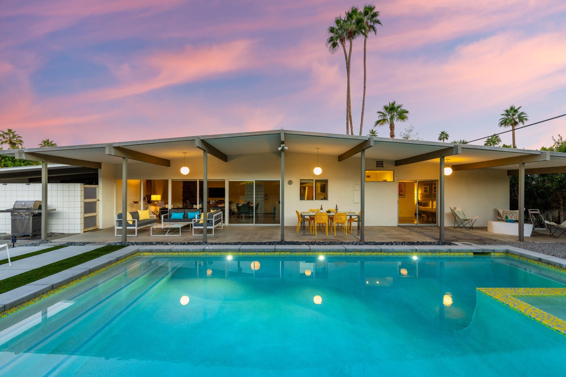 Modern desert retreat with stunning pool under painted desert skies, framed by swaying palms and midcentury architecture.