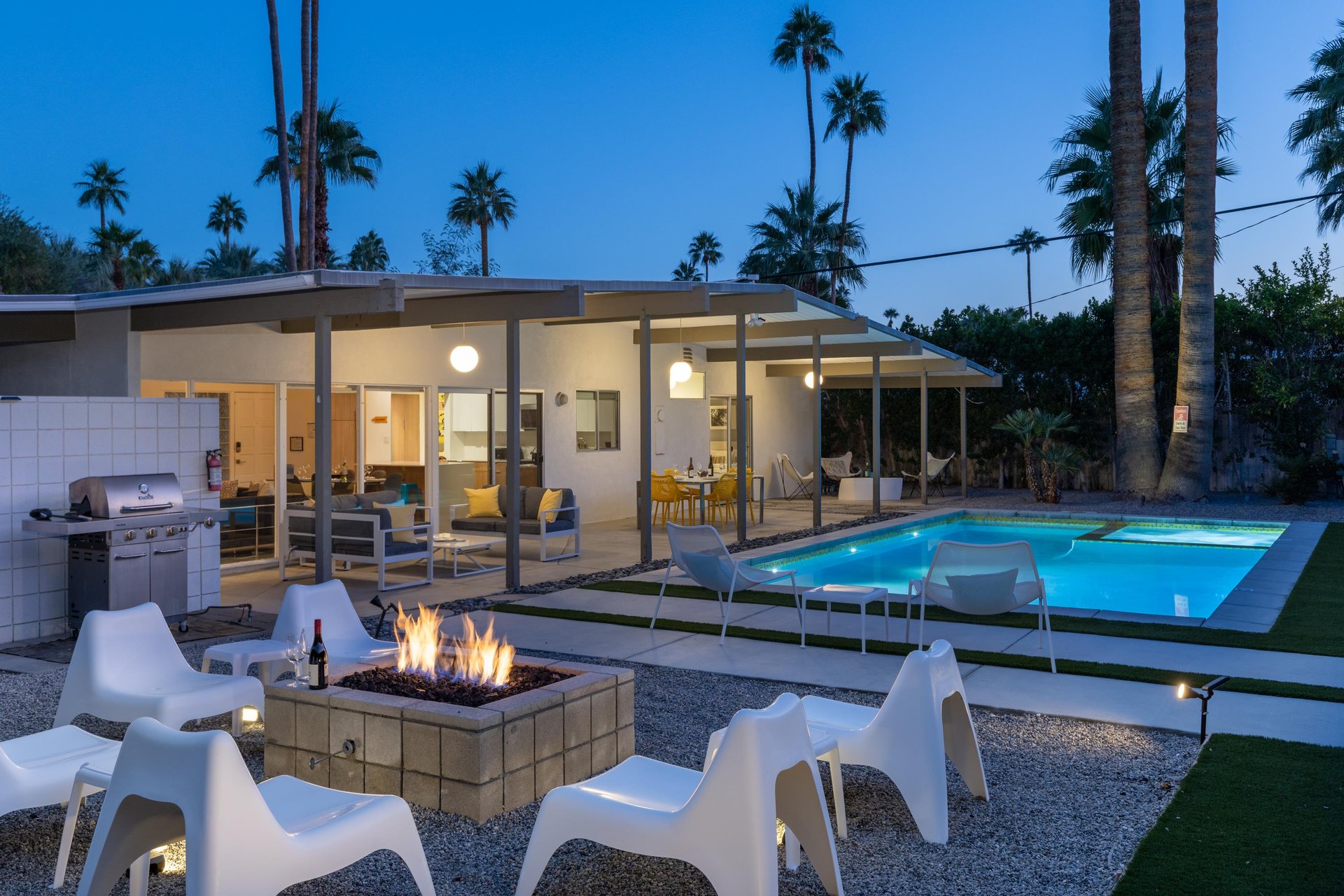 Modern desert retreat with illuminated pool, fire pit seating, and palmstudded surroundings.