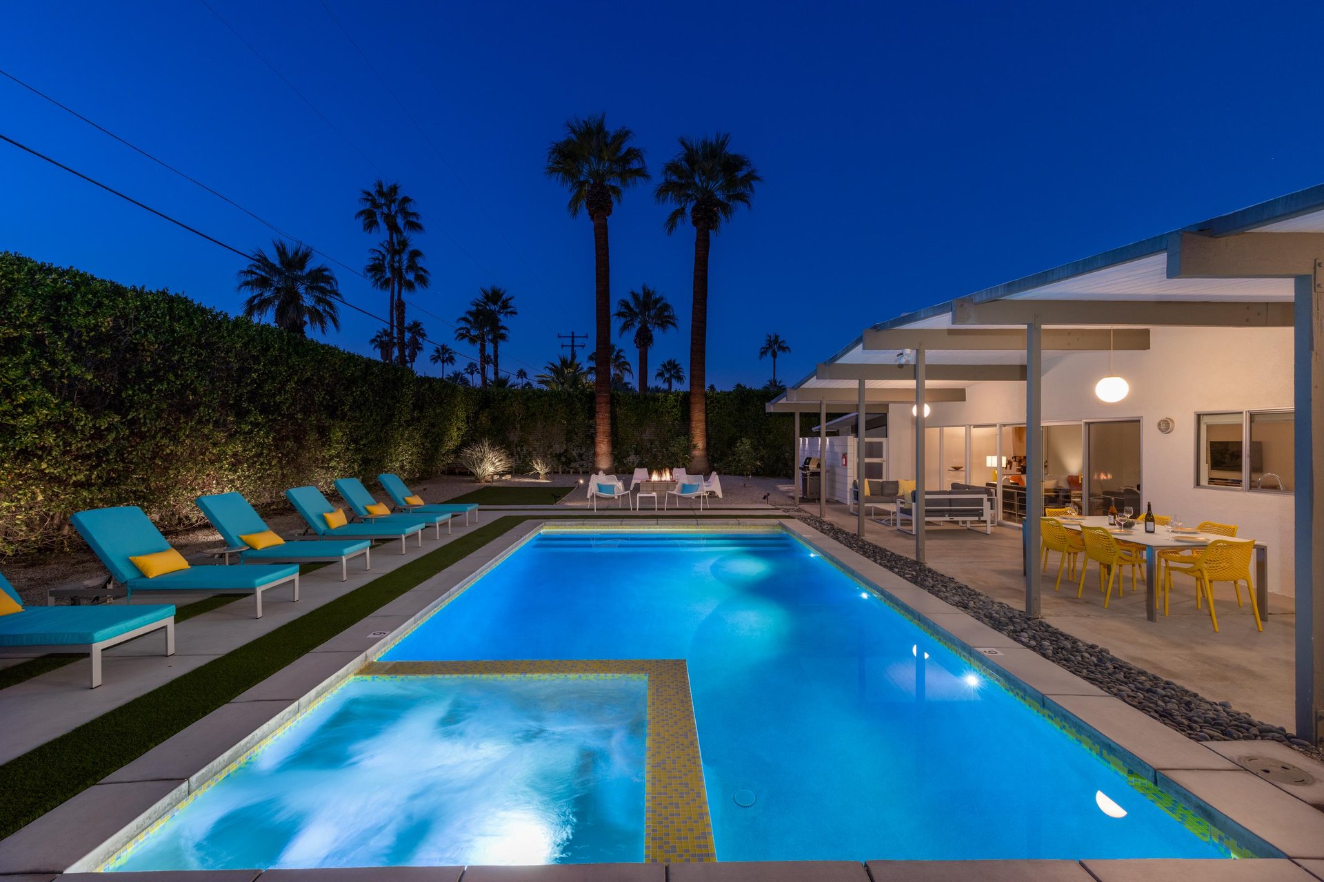 Modern poolside paradise awaits with illuminated waters, loungers, and dining space under towering palms in this desert oasis.