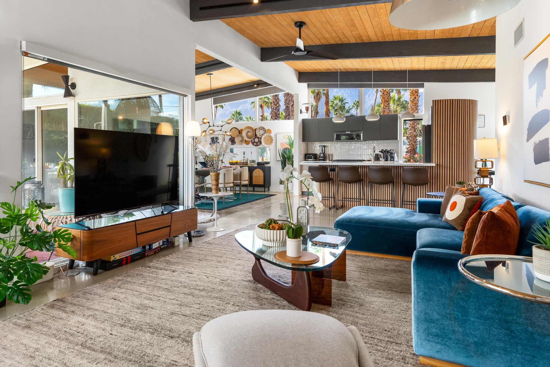 Relax in this stunning midcentury modern living space where rich blue velvet seating meets warm wood tones and desert views beyond.