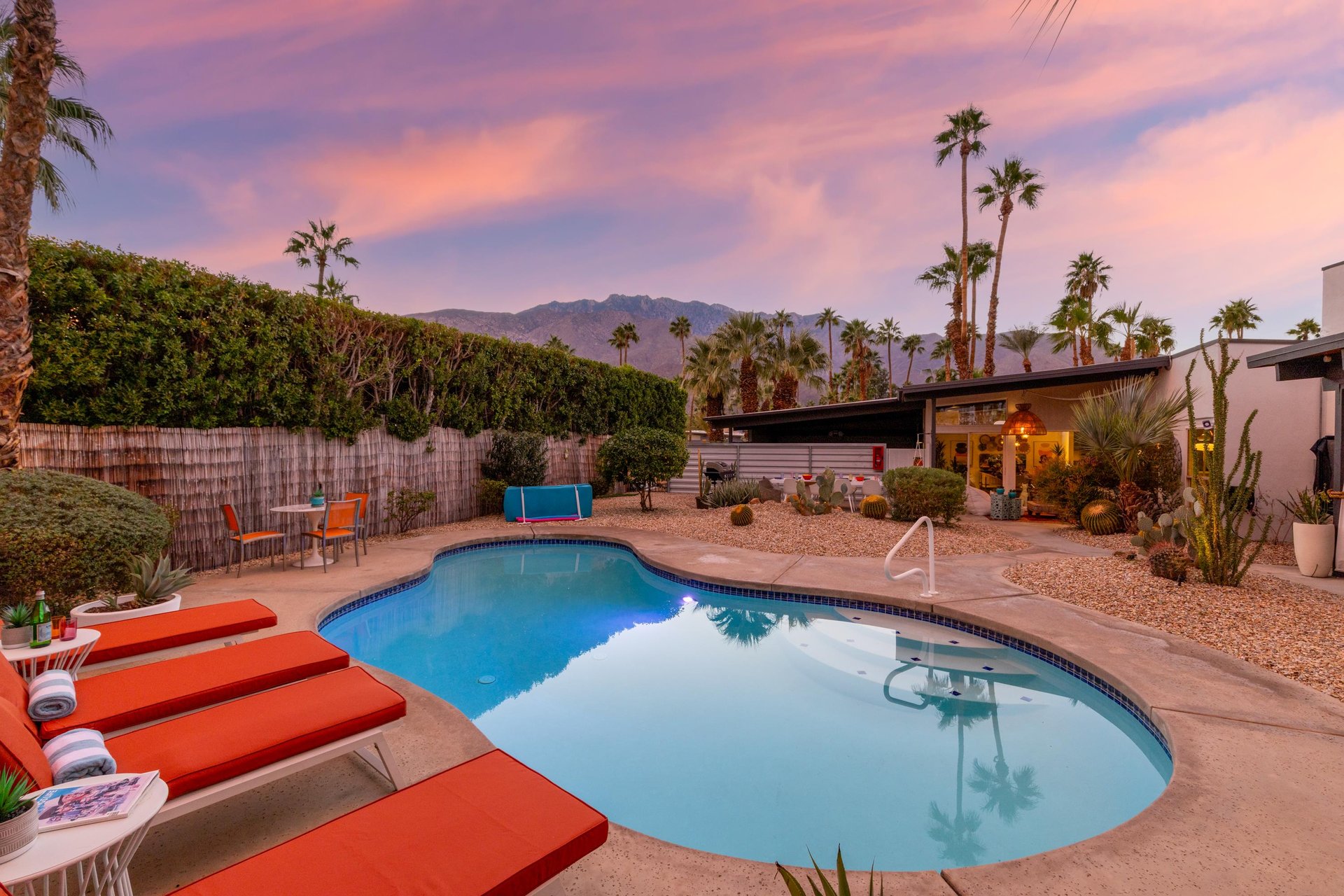 Desert mountain views frame this sparkling pool oasis at sunset, surrounded by mature palm trees and desert landscaping.