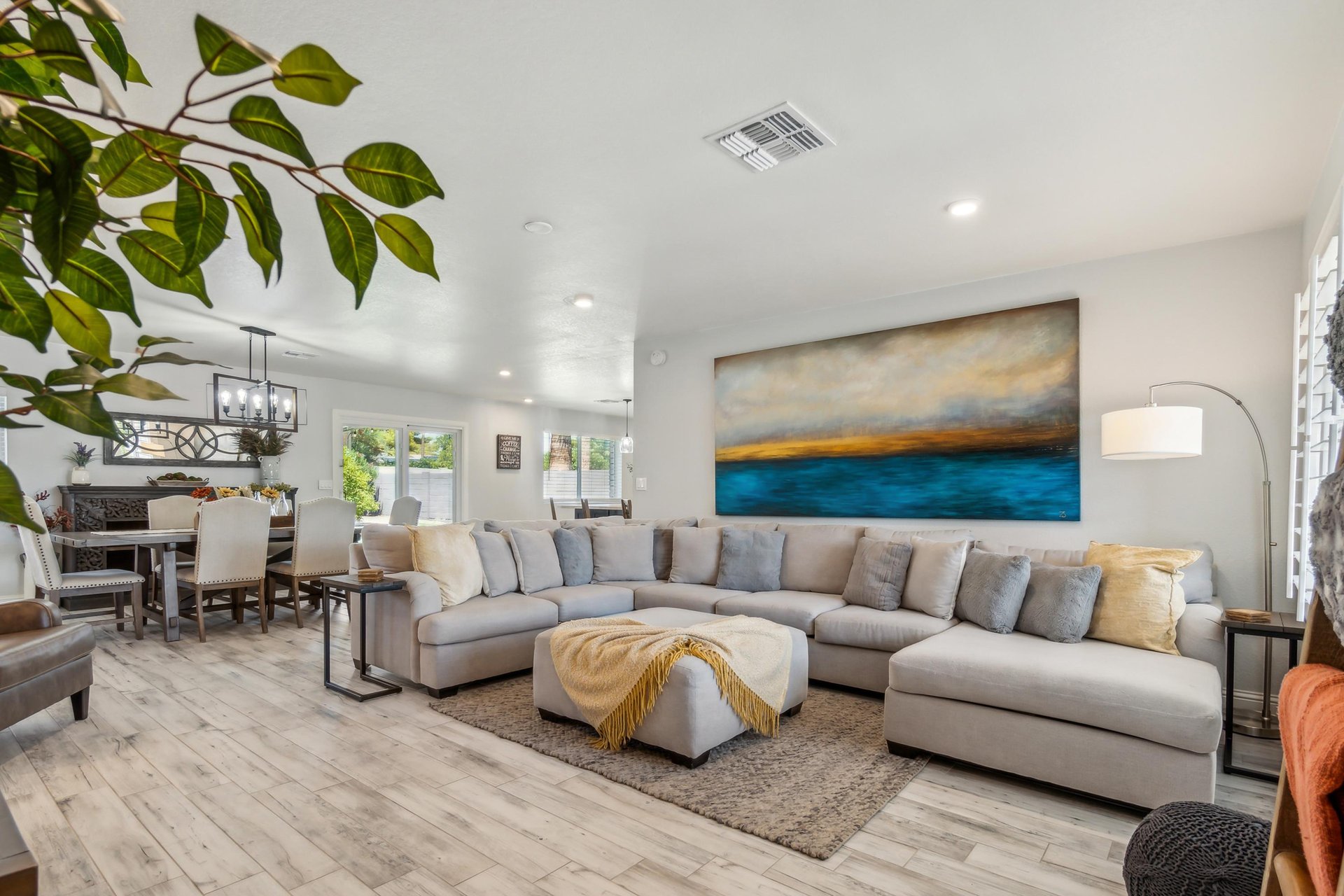 A modern, openconcept living and dining area. A large gray sectional sofa with pillows and a cushioned ottoman.