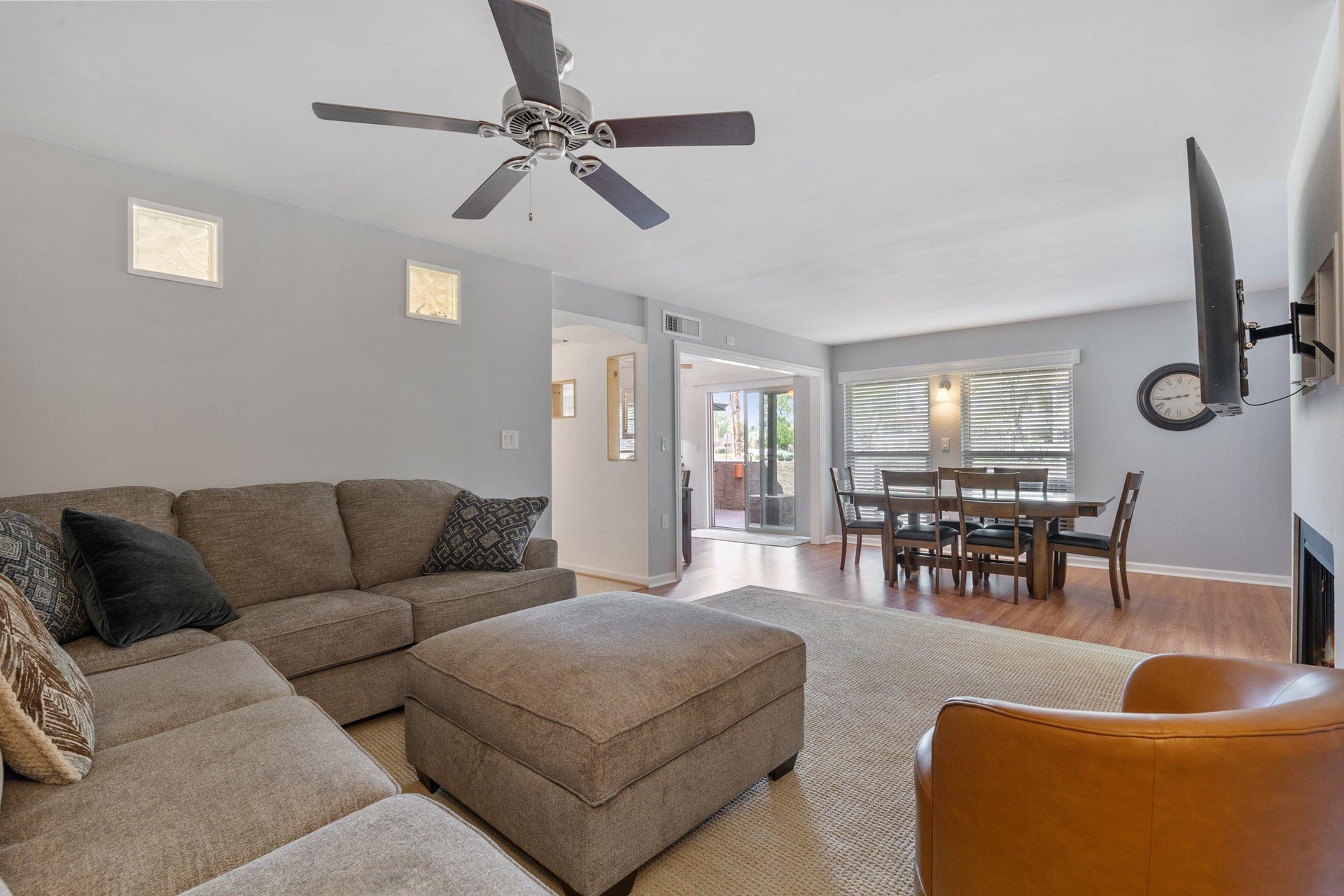The cozy couch sits below a ceiling fan and in front of the living room fire place and large Smart TV.