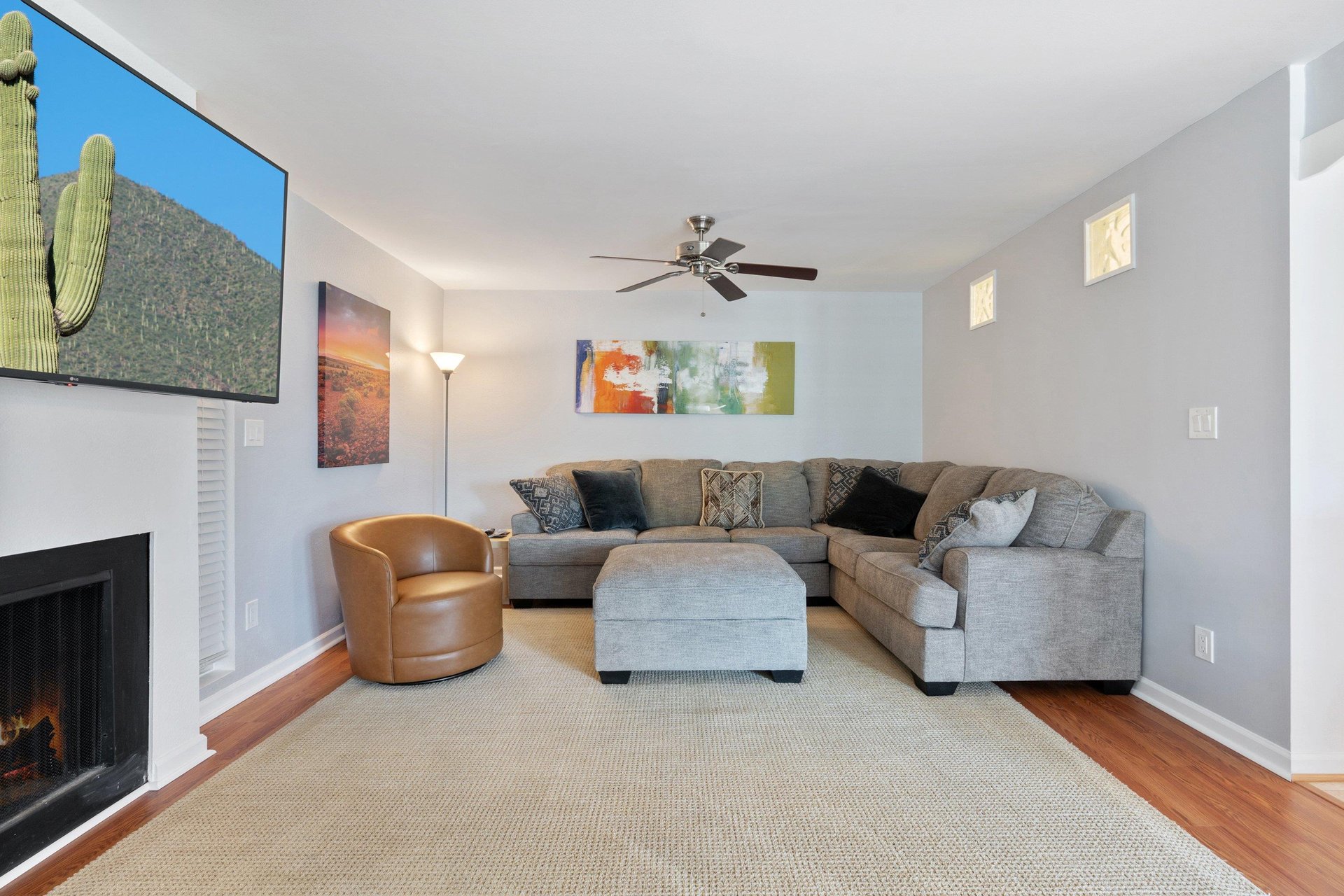 The cozy couch sits below a ceiling fan and in front of the living room fire place and large Smart TV.
