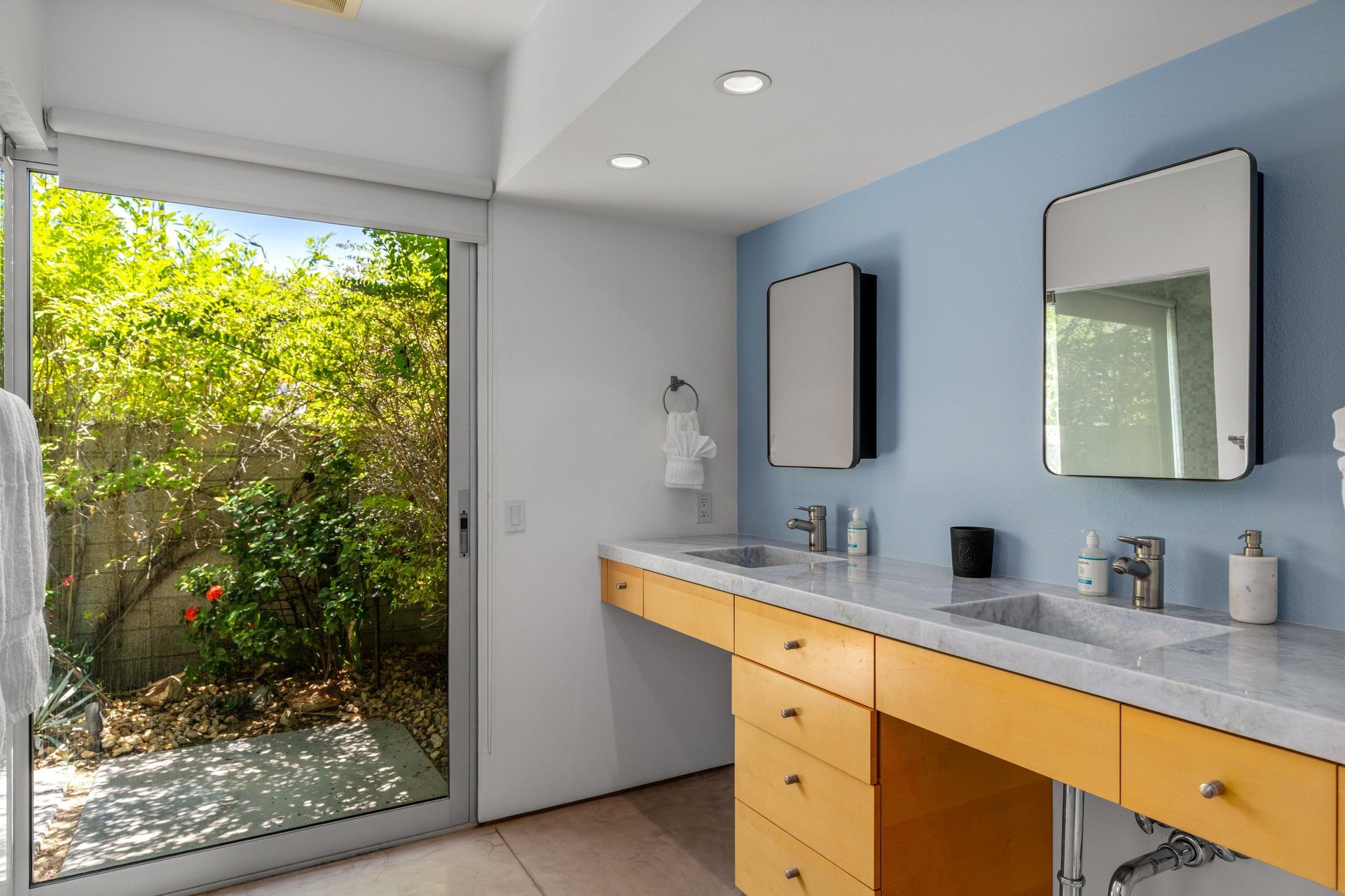 Stunning primary bathroom with dual vanity sink, large sliding doors with natural lighting, and standalone shower with its own sliding door to turn it into an indooroutdoor shower.