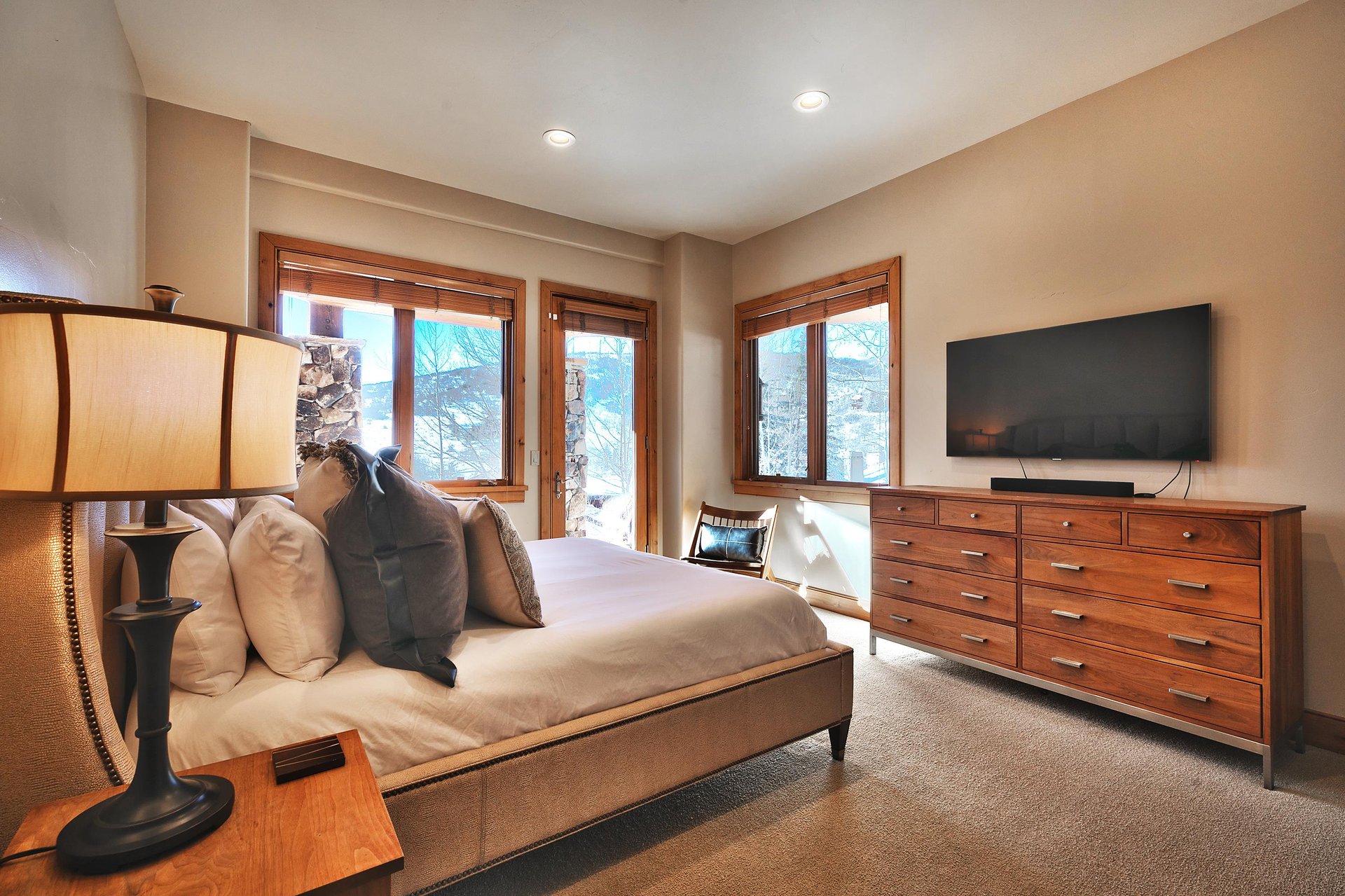 Fourth bedroom with king bed, upholstered bedframe and headboard, wooden dresser, wall mounted TV and glass door to a patio.