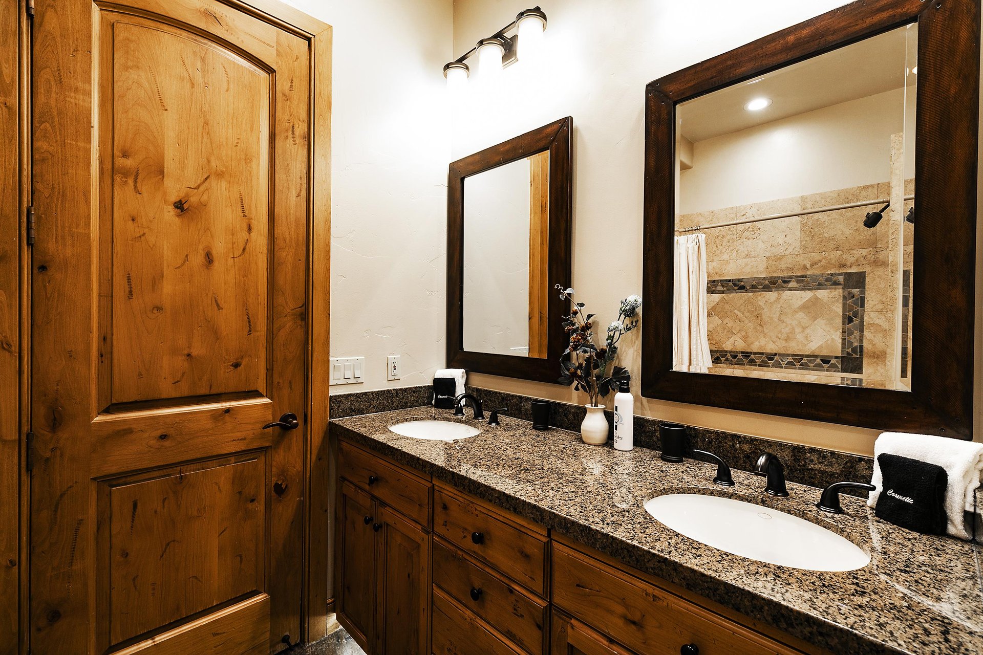 Dual sink, medium toned wood vanity with granite countertops, two mirrors and two lights.