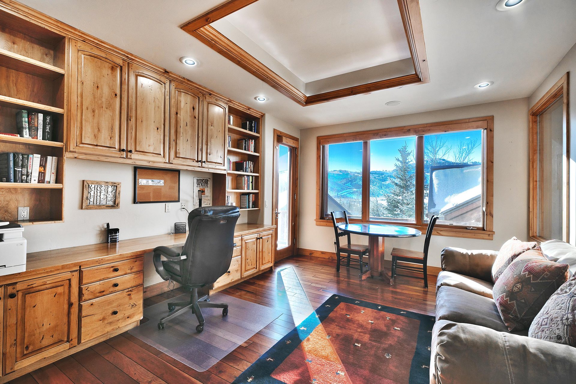 Private office space with builtin desk, black roller chair, and round table with seating for two in front of a large window.
