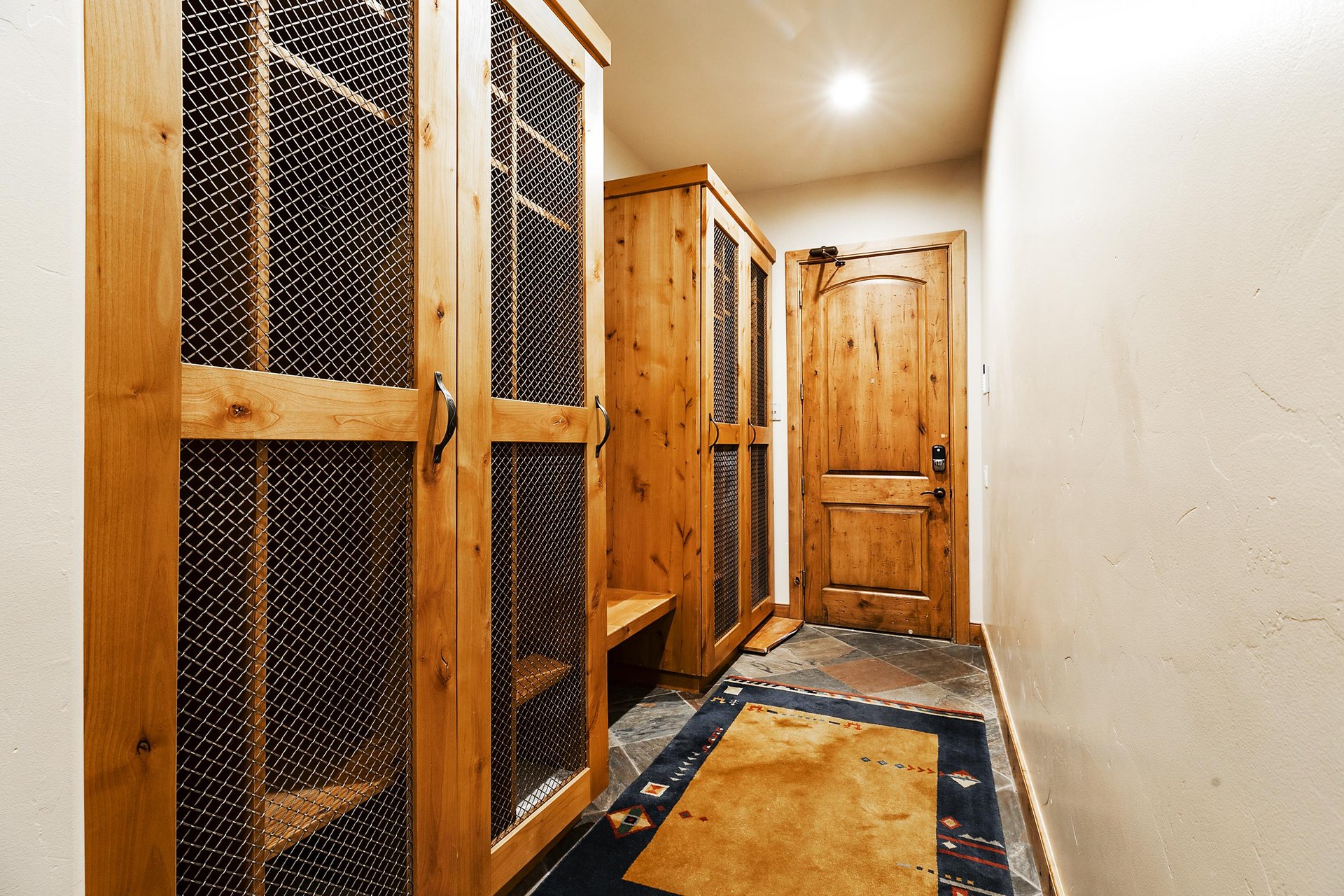Tall wooden ski lockers with wooden bench, slate floors with a runner on them, and access door to the garage.
