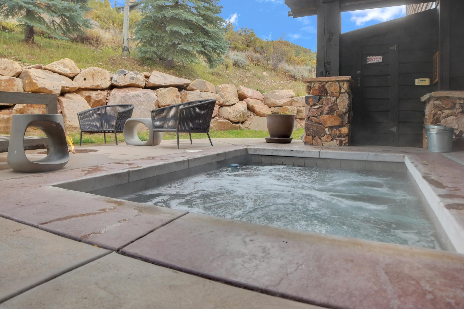 Bubbling hot tub next to an inground fire pit with comfortable seating around the fire and a gorgeous private yard.