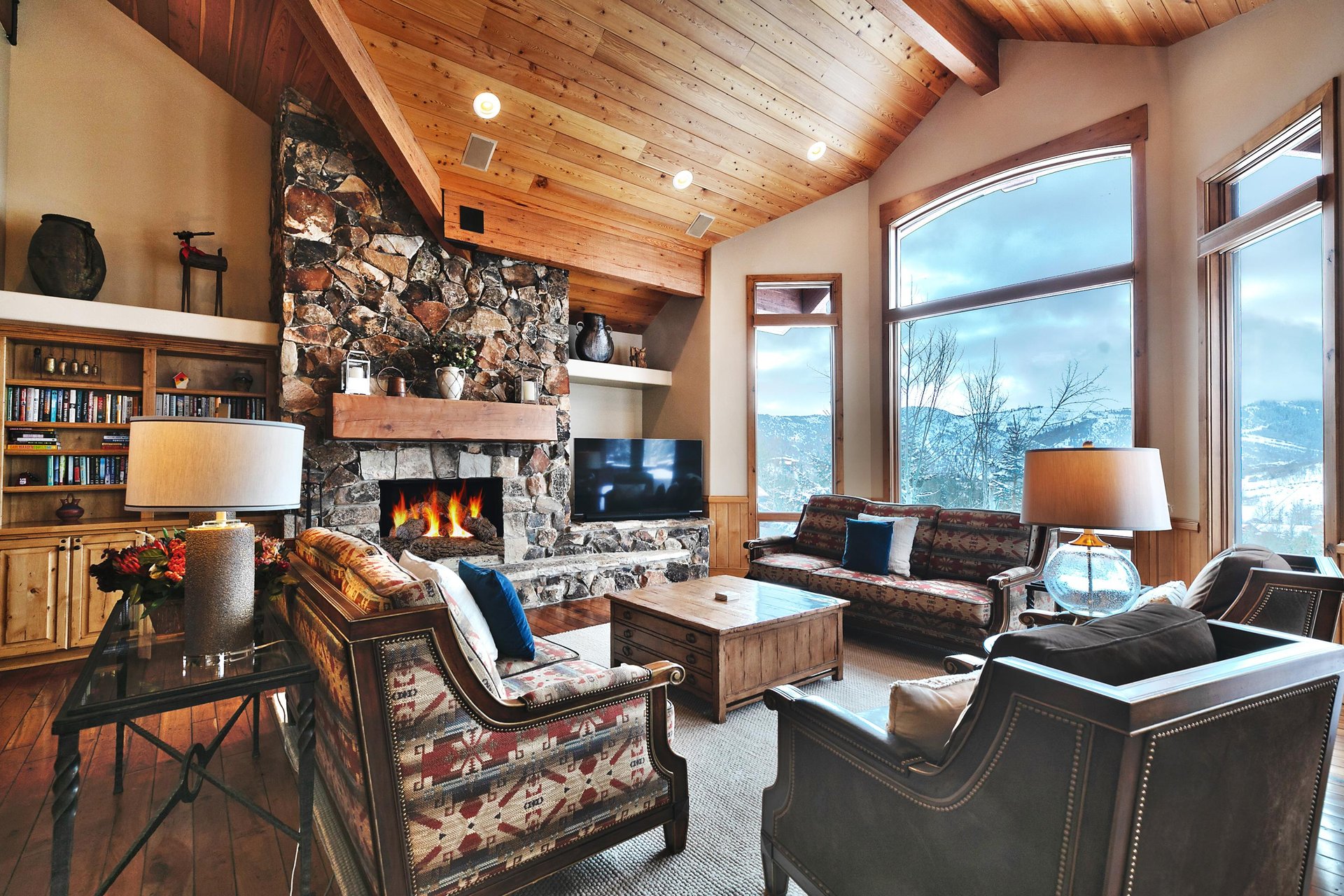 The living room has a wood burning fireplace with floor to ceiling stone surround, Smart TV, 2 couches, and 2 club chairs.