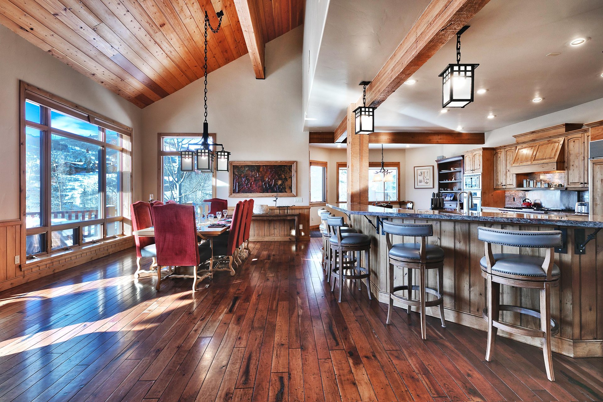 Dining room with 6 large red velvet upholstered chairs, wooden table, and impressive kitchen breakfast bar with 6 stools.