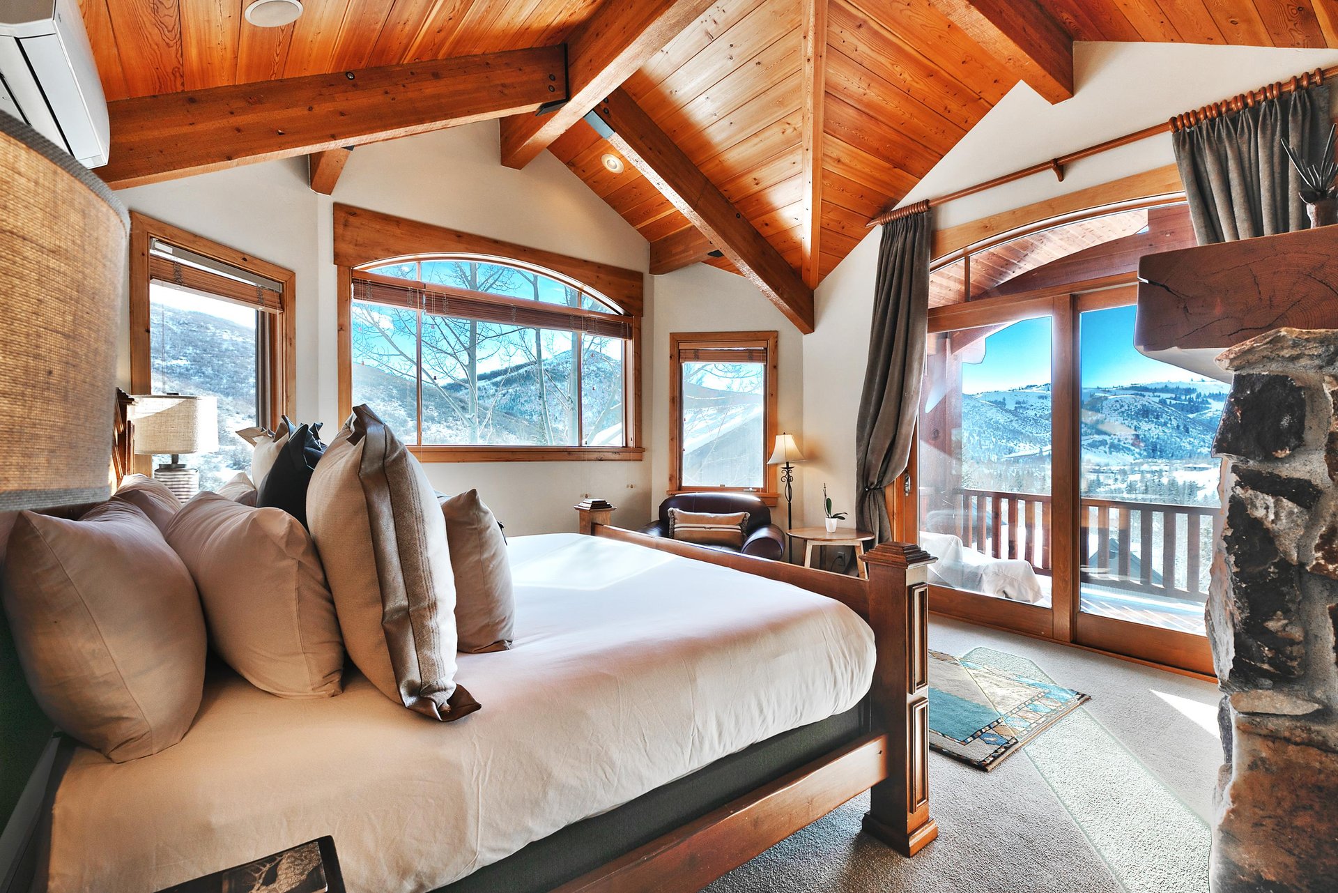 First main bedroom with vaulted wood beam ceilings, 4 poster bed with white linens, and sliding patio doors.