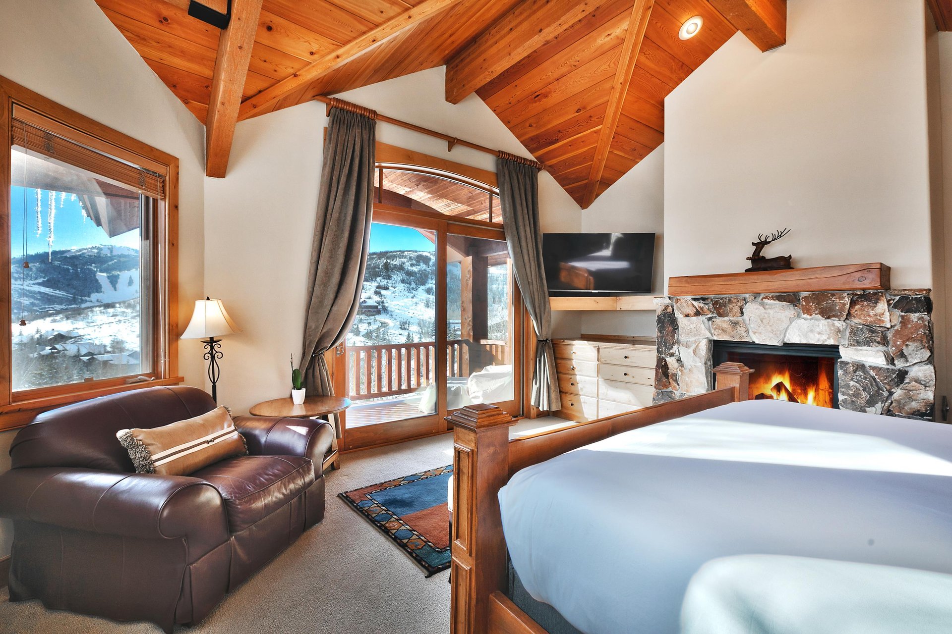 A four poster bed next to a cozy gas fireplace, wall mounted TV, dresser, and sliding glass doors leading to a private patio.