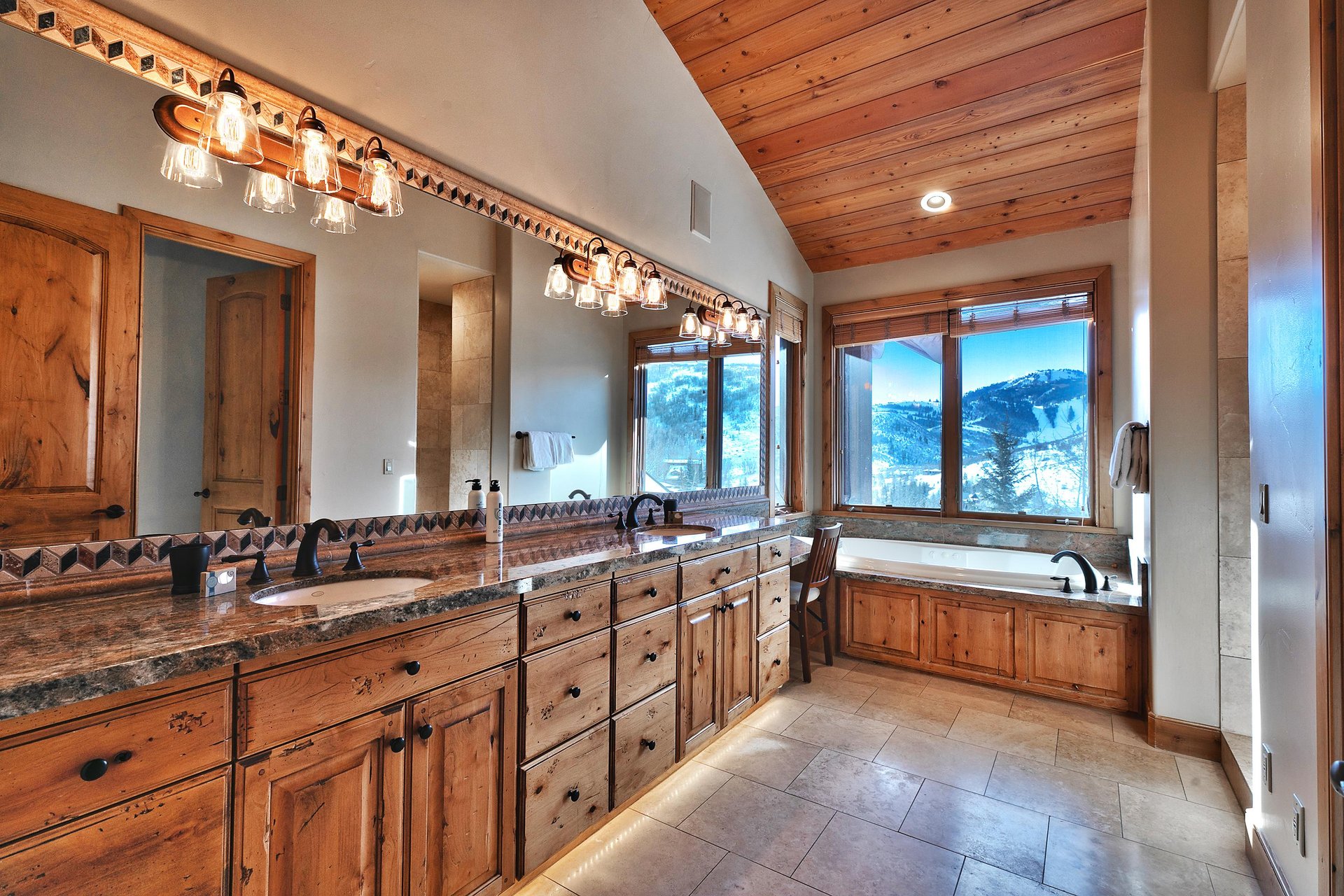 Ensuite bathroom with long dual sink vanity and mirror, granite countertops and three vanity lights, next to a soaker tub.