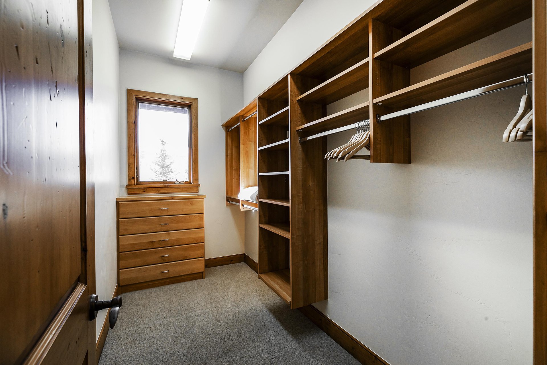Spacious walk in closet off the first bedroom with built in shelves and hanger rods, wooden dresser, and window.