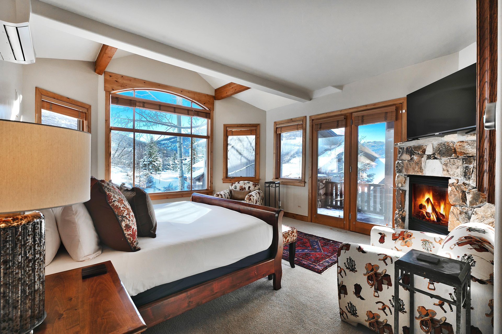 Second bedroom suite with king bed, many windows framing snowy mountains, gas fireplace, and two cowboy print accent chairs