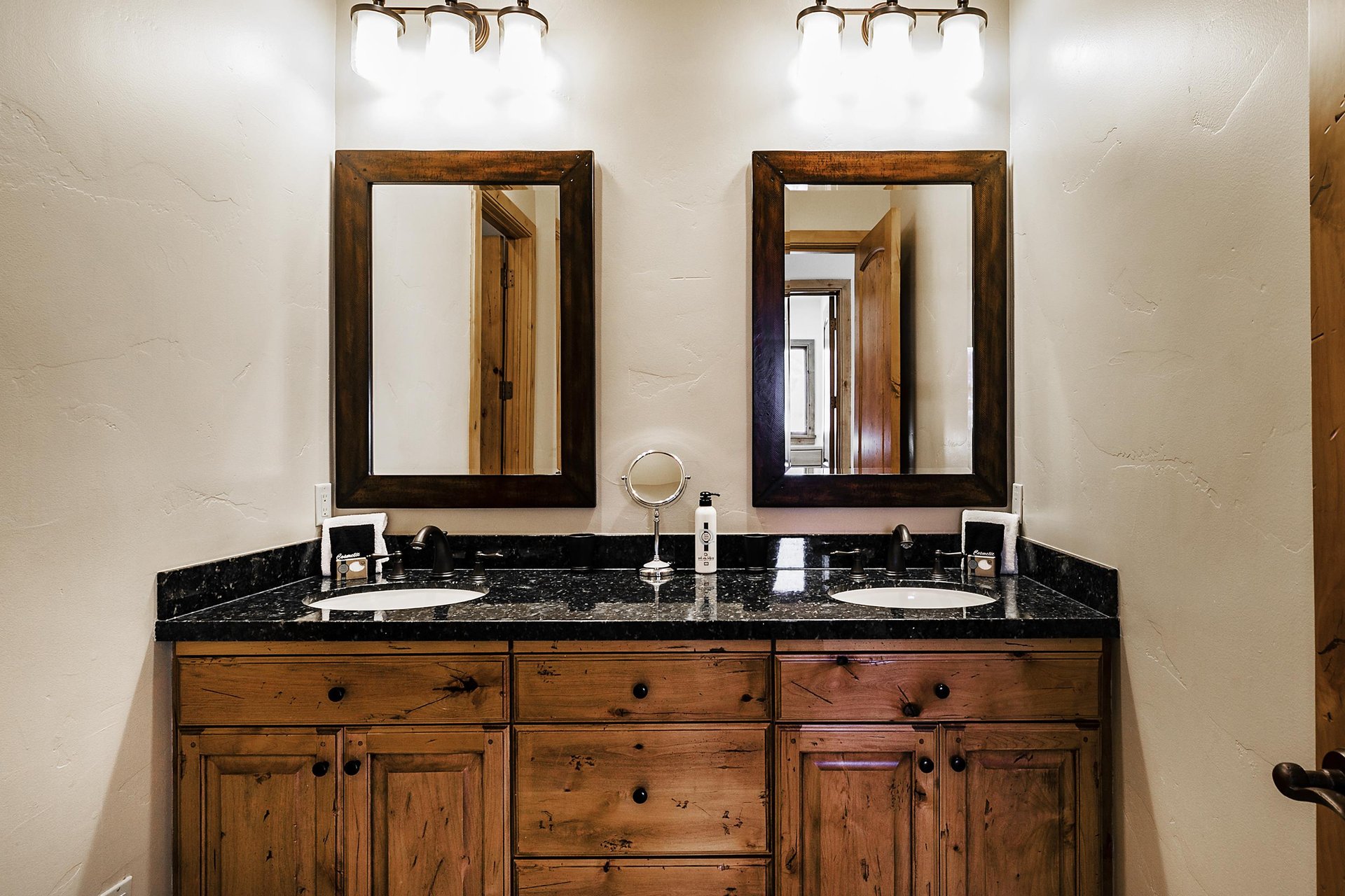 The bathroom has a dual sink medium tone wooden vanity with black granite counter, two mirrors, and two vanity lights.