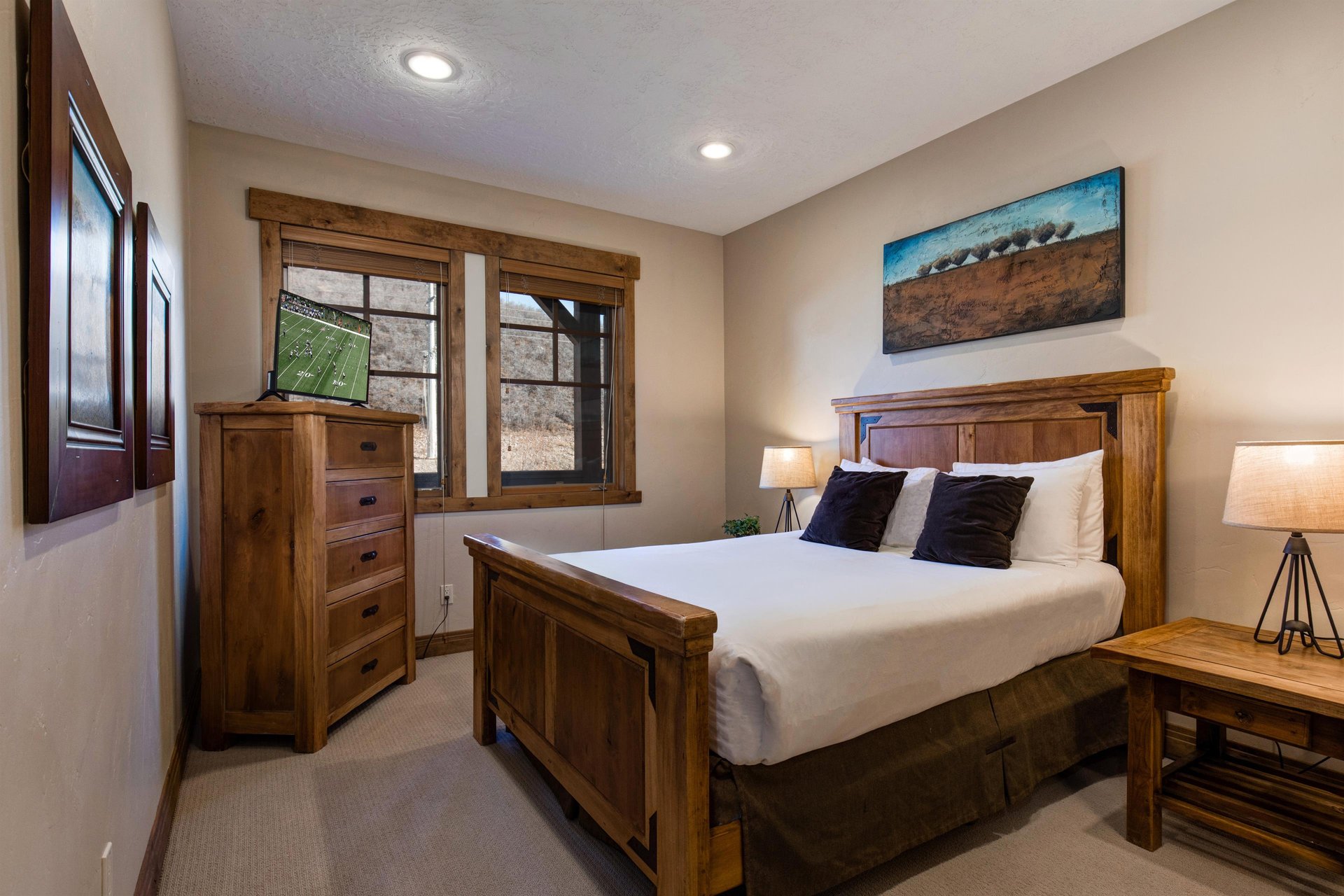 Relax in your cozy bedroom featuring rustic wood furnishings, crisp white linens, and modern amenities including a TV for your evening entertainment.