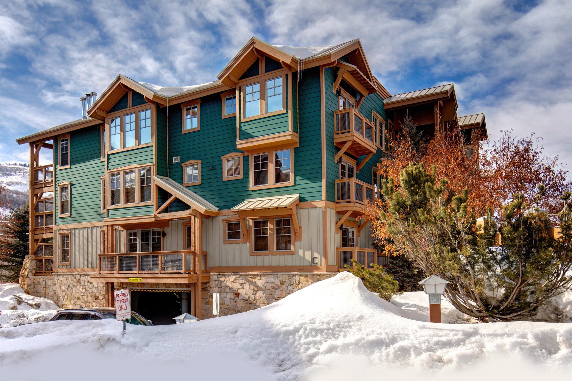 Striking multistory vacation rental building with distinctive green and wood exterior, stone foundation, and mountain lodge architecture.