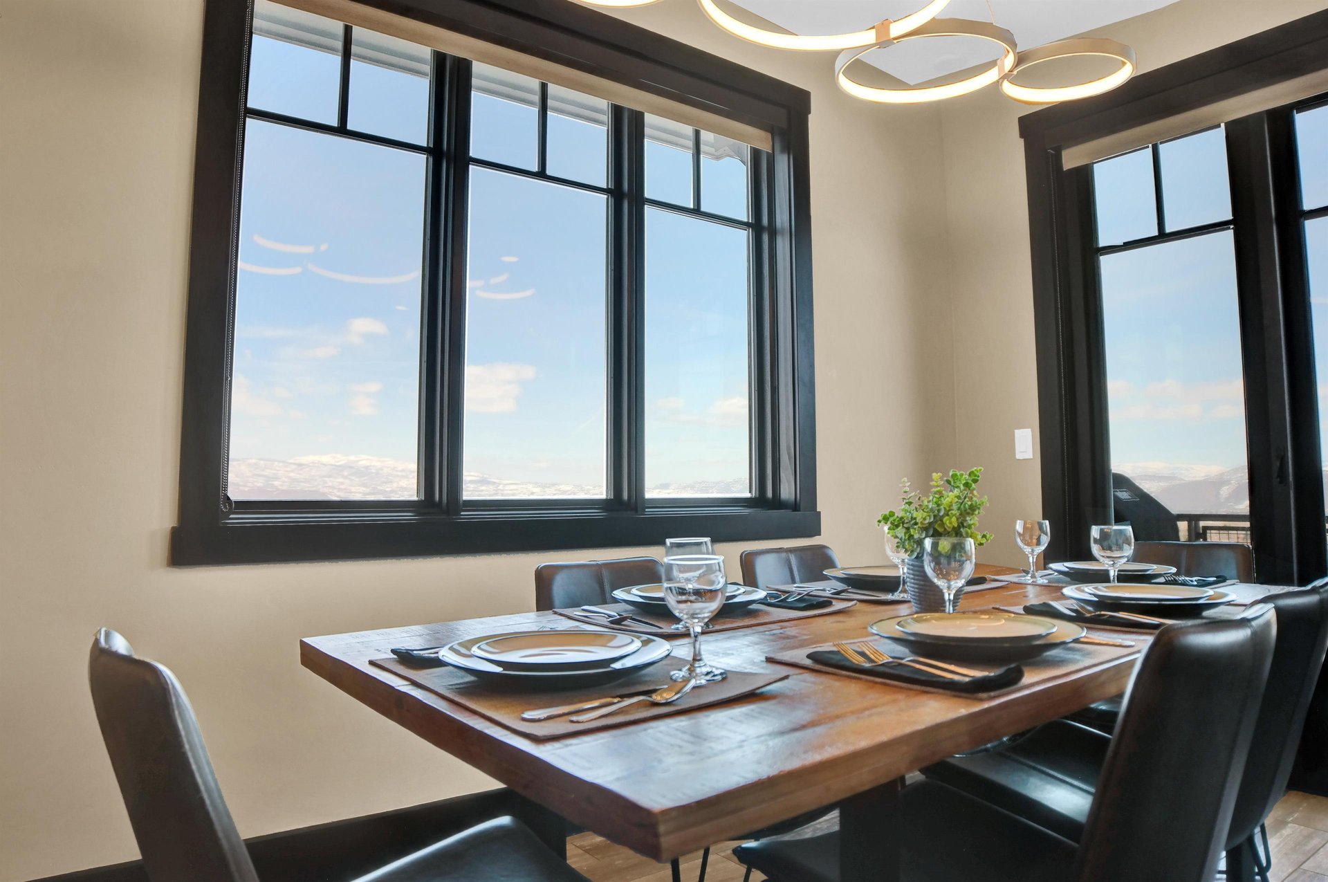 Wood dining table with leather chairs and a large window with snowy mountain views beyond.