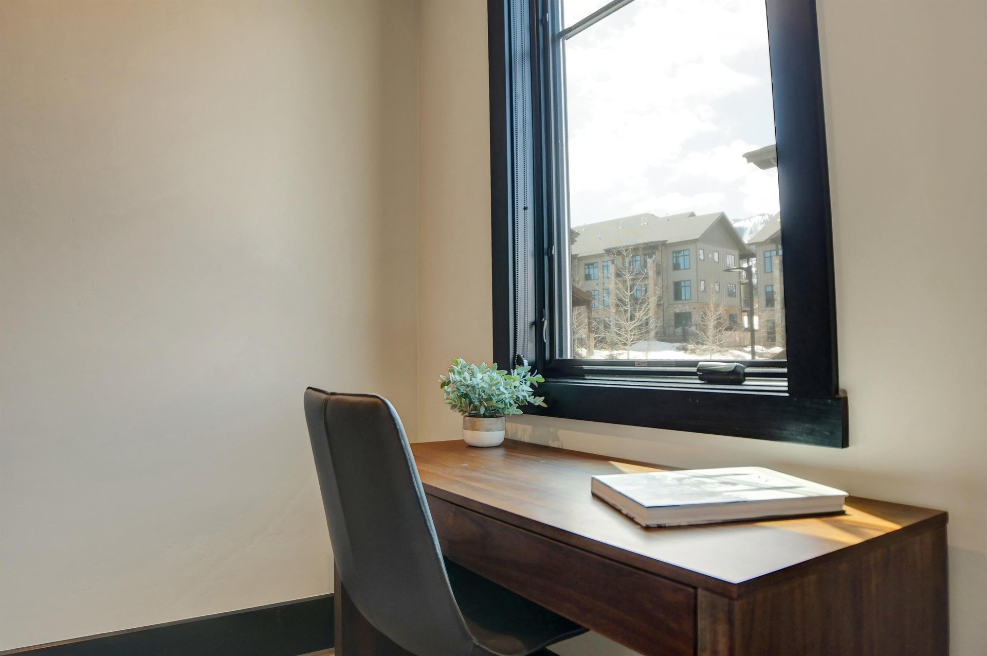 An office nook with wooden desk with grey leather chair in front of a window.
