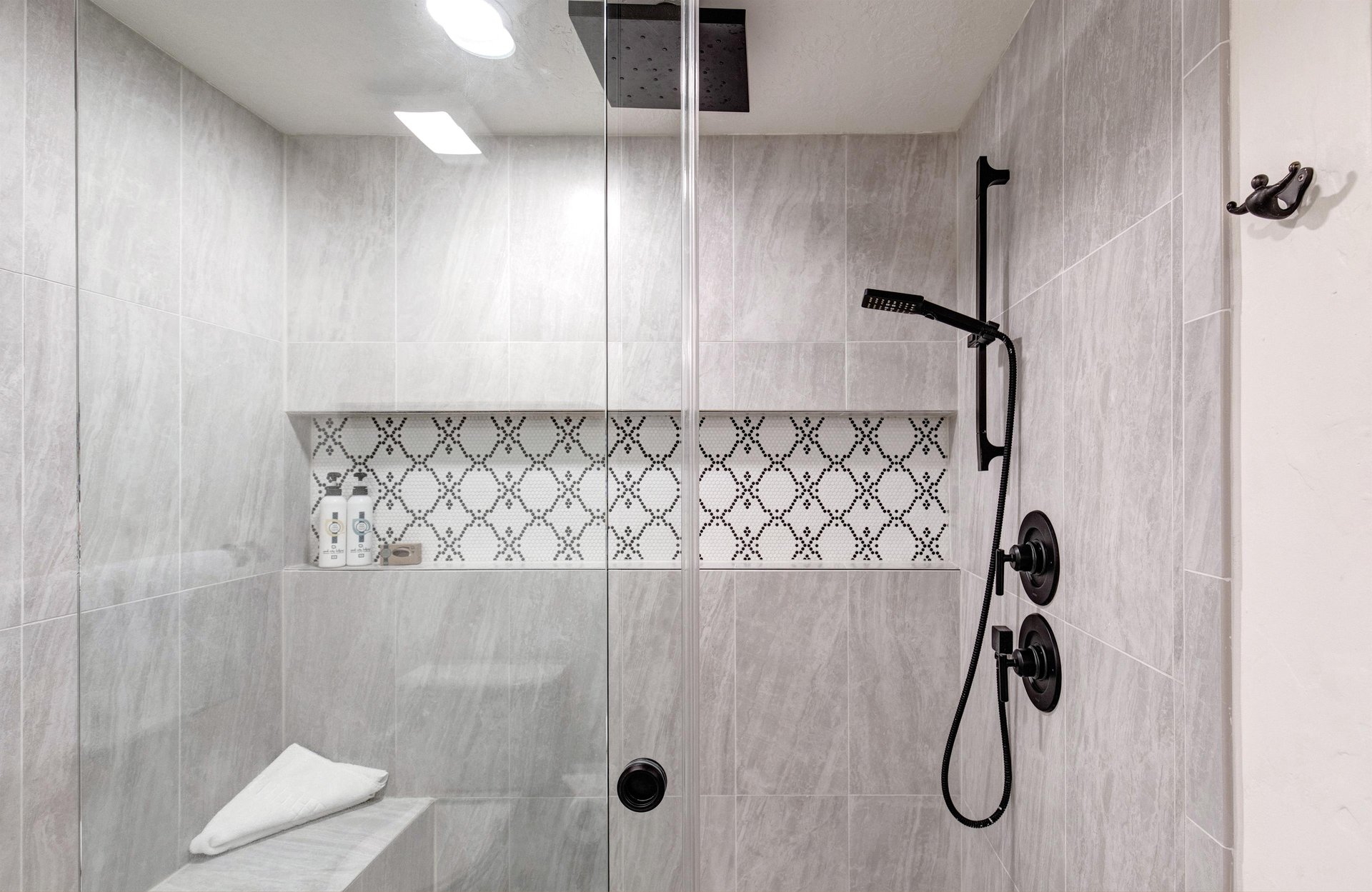 The en suite bathroom offers a spalike shower, where a dual rainfall and handheld system meets elegant mosaic tile.