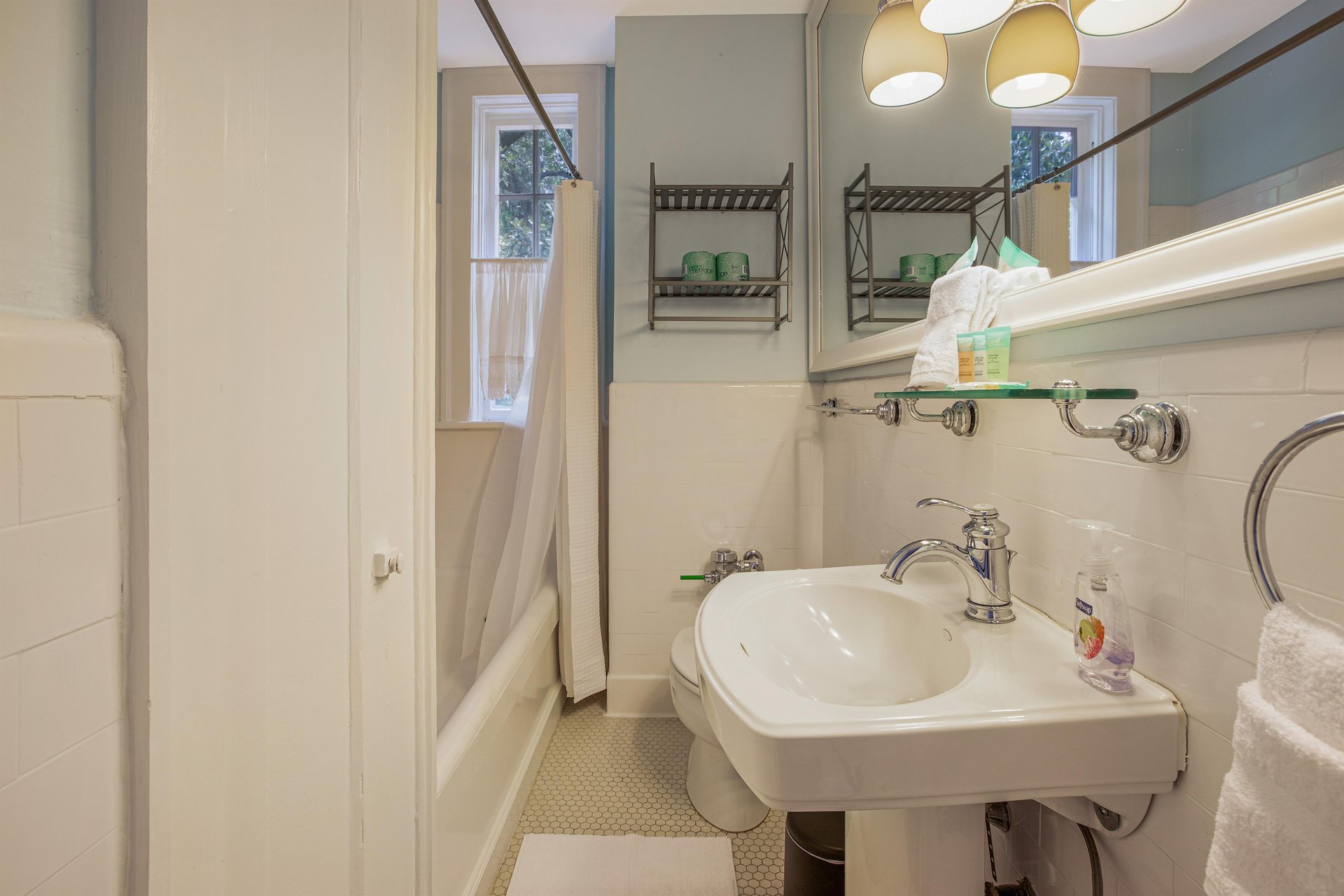 The bathroom faces Forsyth Park, and features an original pedestal sink, storage, and showertub combination.