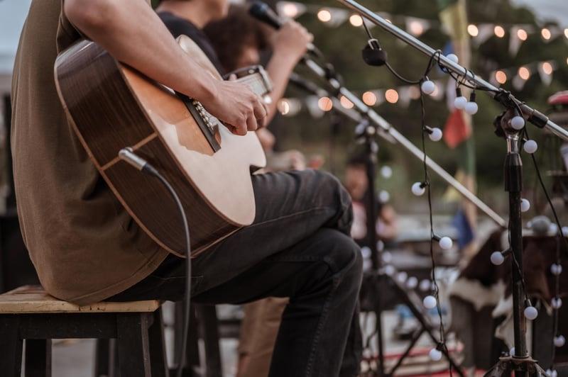 Intimate acoustic performances under the stars — Park City Song Summit brings worldclass artists and meaningful conversations to Park City each summer. Musician playing acoustic guitar on outdoor stage with string lights Park City Song Summit