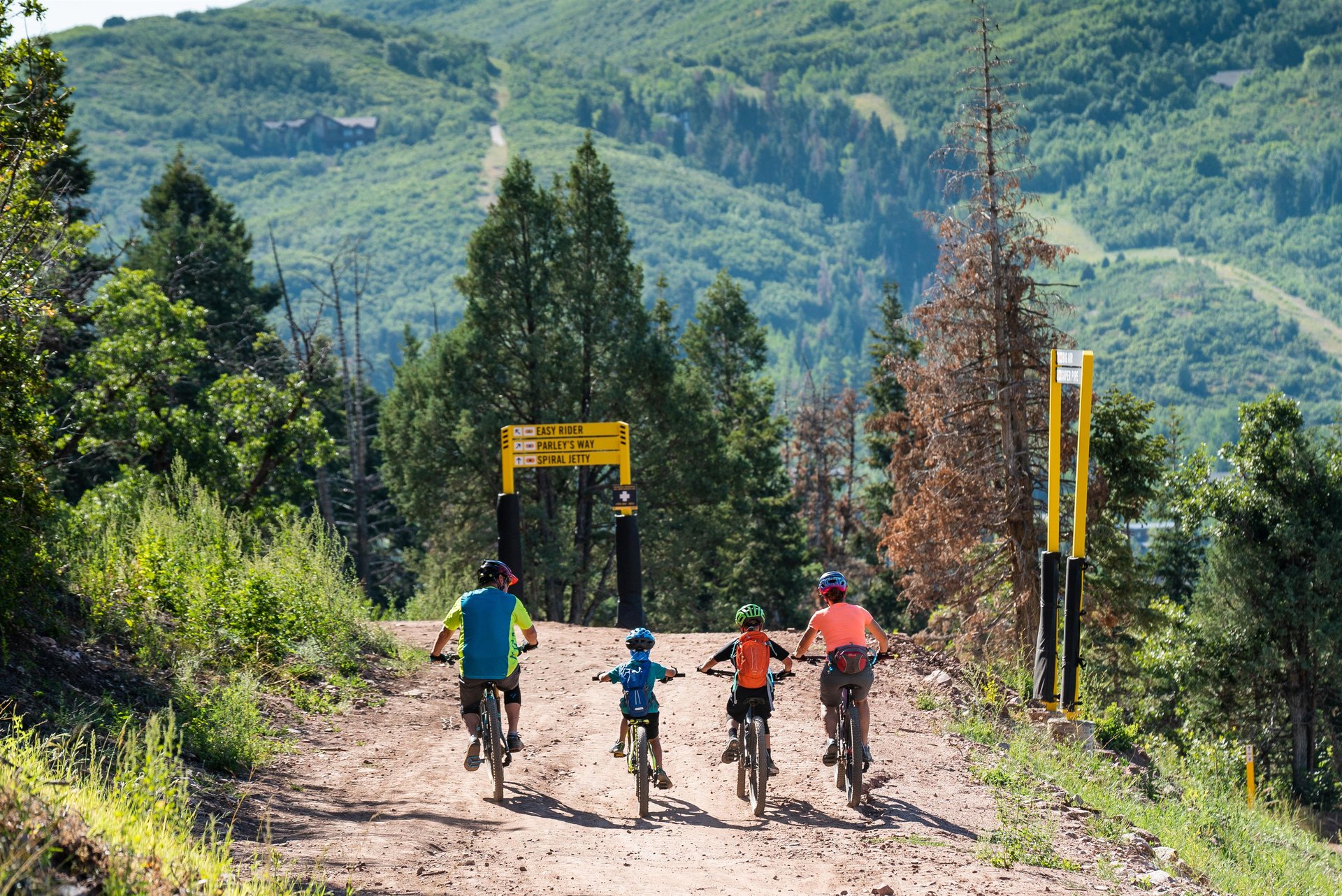 Family of four mountain biking past trail signs at Woodward Park City summer Utah