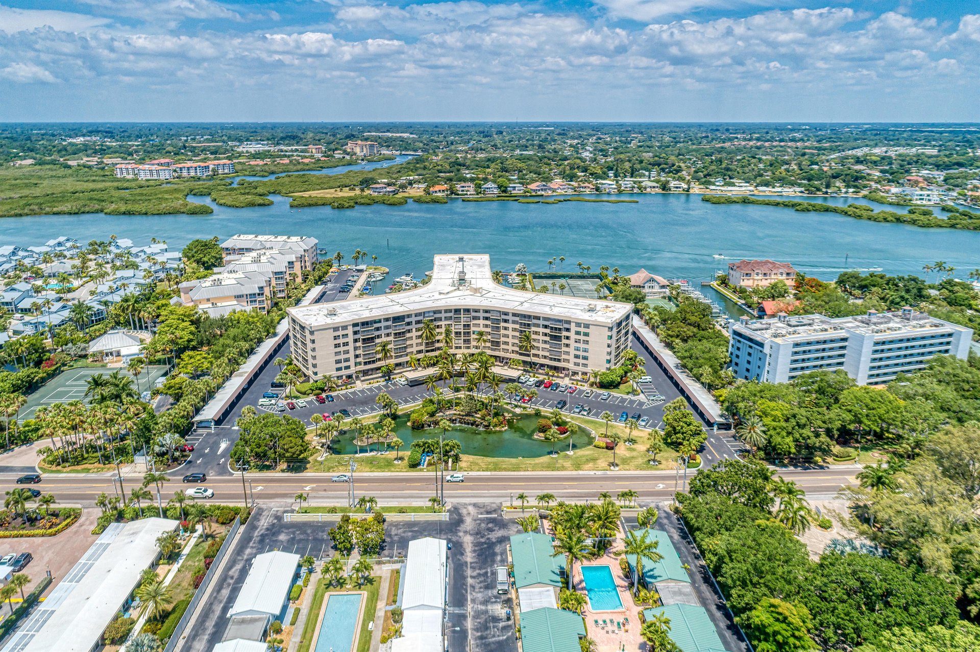 Aerial view of a waterfront resort property with expansive grounds, nestled between tranquil waters and lush tropical landscaping.
