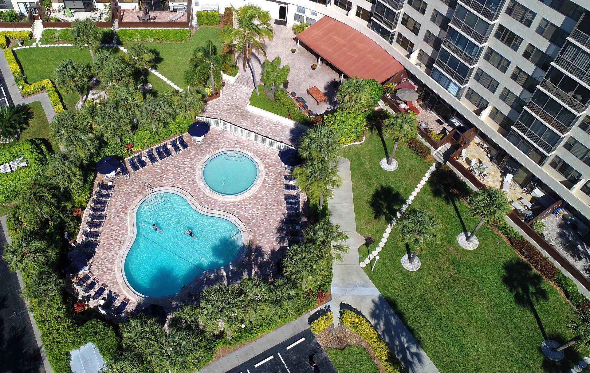 Aerial view showcasing the resortstyle pool area with tropical landscaping, surrounded by modern apartment buildings and lush green spaces.