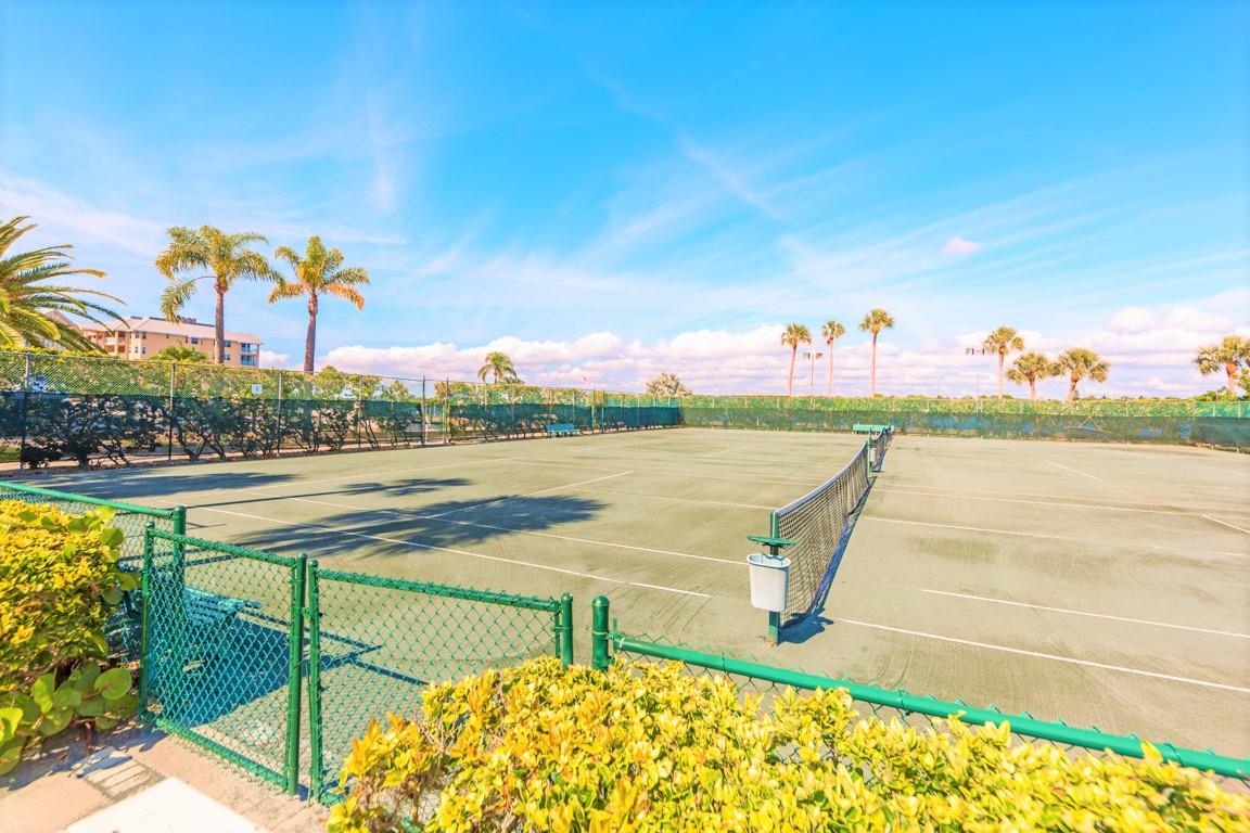 Tennis court surrounded by tropical palms and lush landscaping under beautiful blue skies.