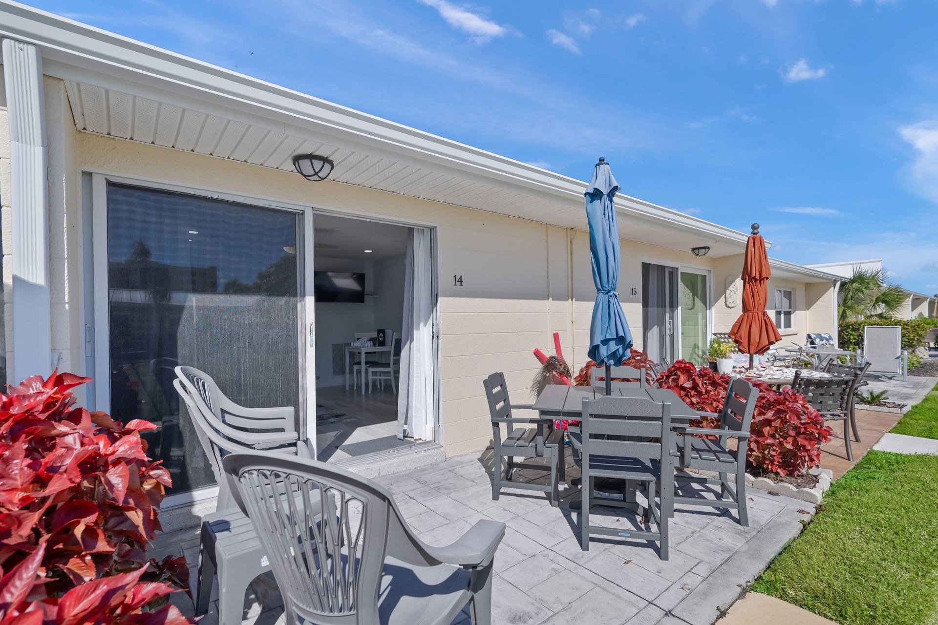 Step onto your private patio where vibrant tropical plants frame outdoor dining under bright blue skies.